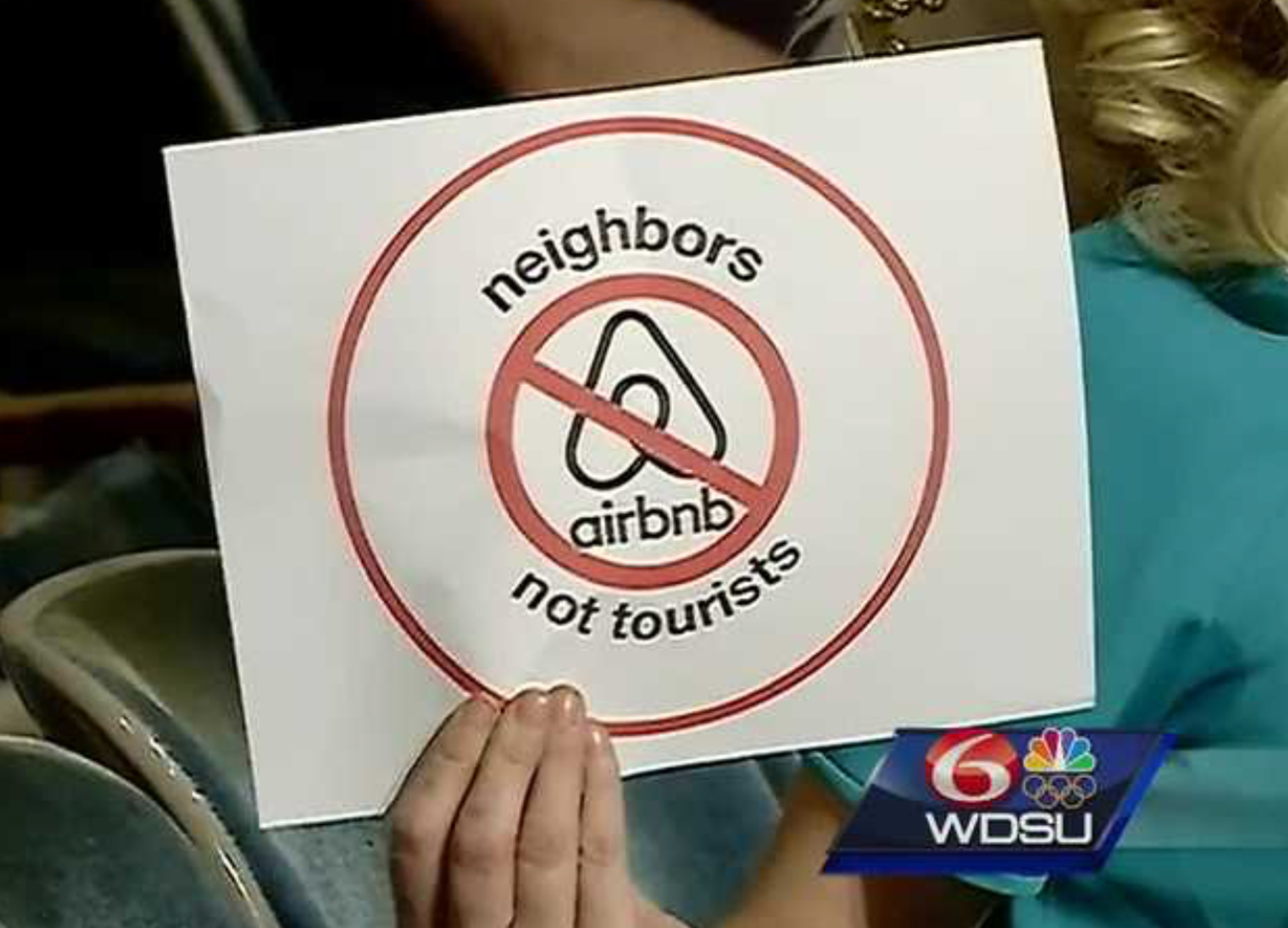 WDSU News screenshot of a woman holding up a "Neighbors Not Tourists, No Airbnb" sign