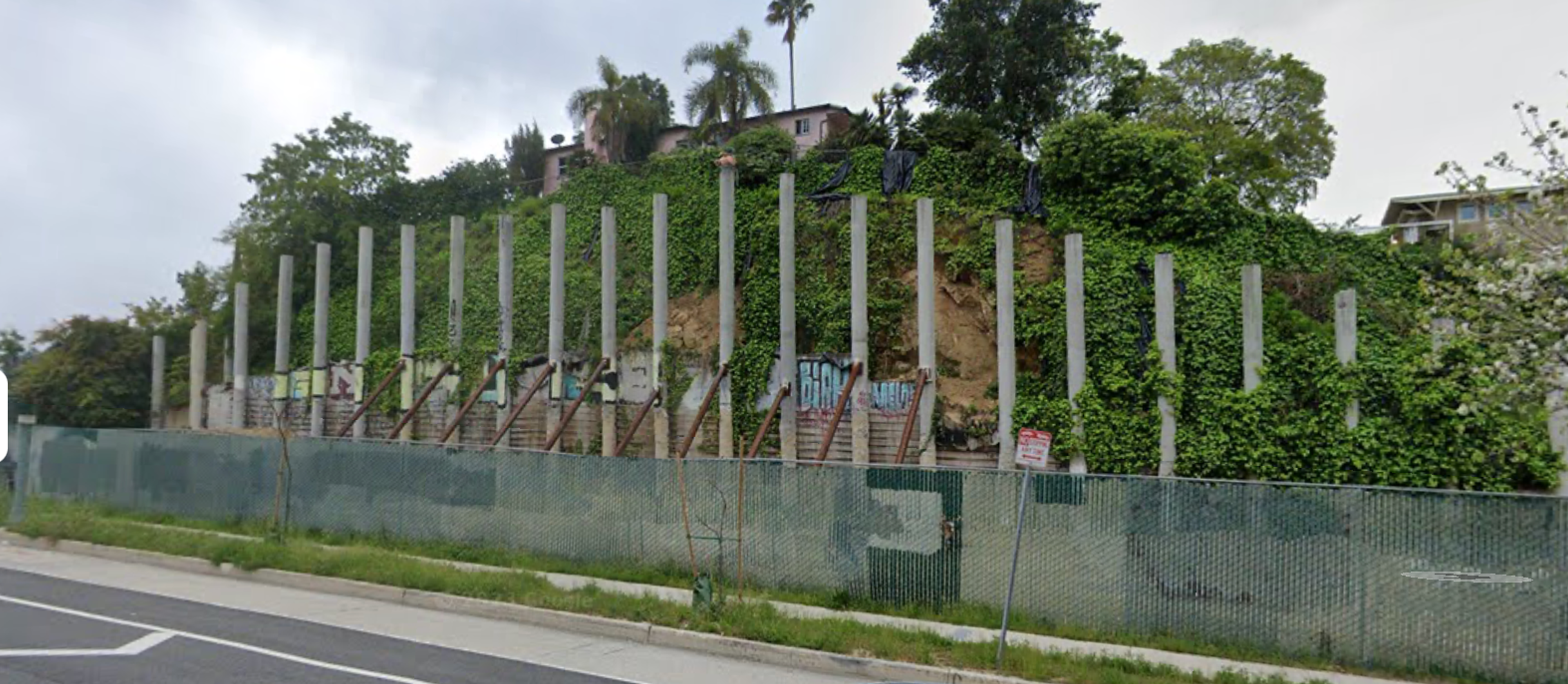 Picture of "Pillarhenge", which is an undeveloped lot with over twenty pillars from an abandoned project. The lot is behind construction fencing and has some graffiti tags.