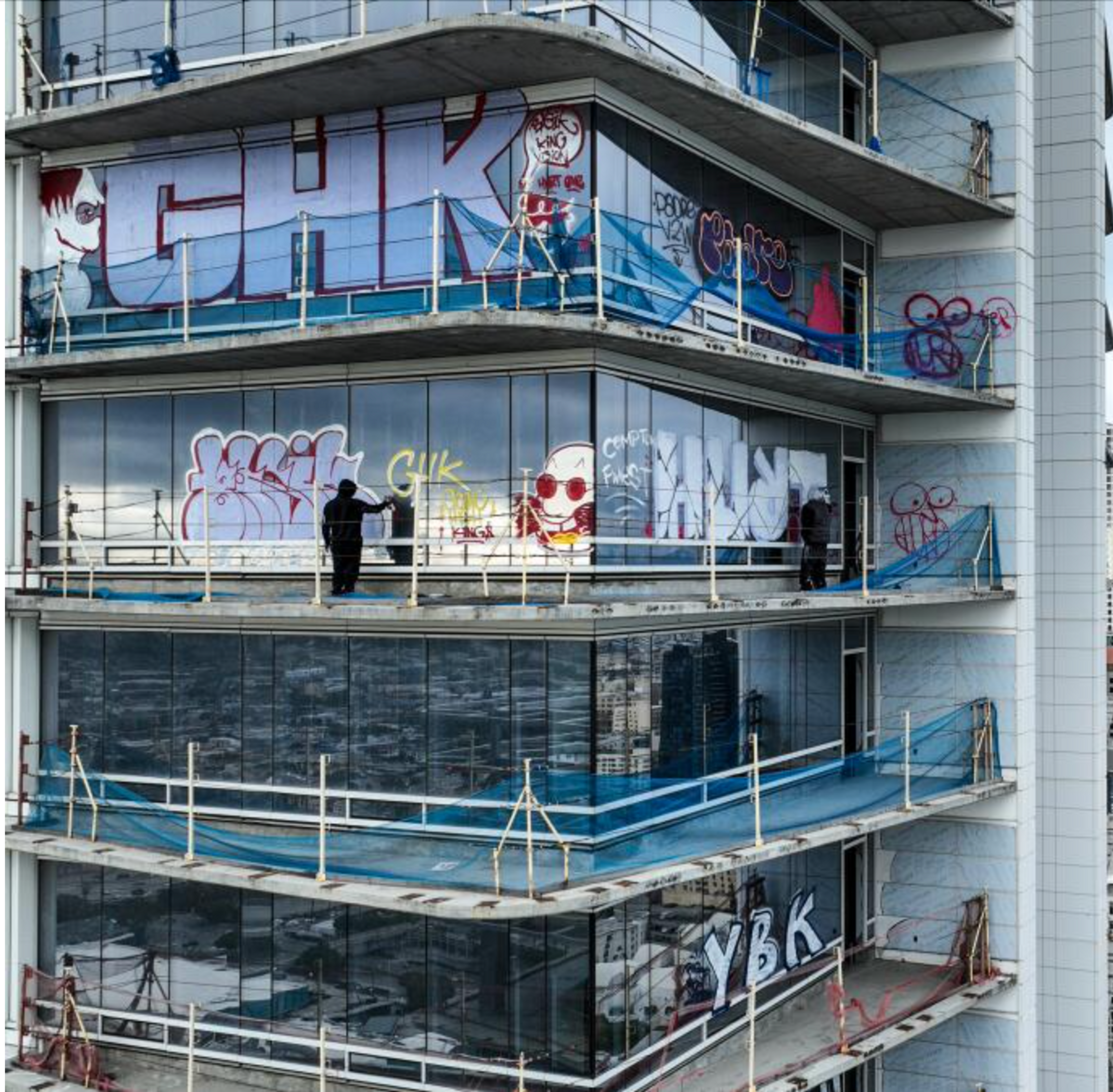 Photo courtesy of the LA Times. Shows a tagger spray painting the heavily tagged Oceanwide Plaza tower. Five stories are visible.