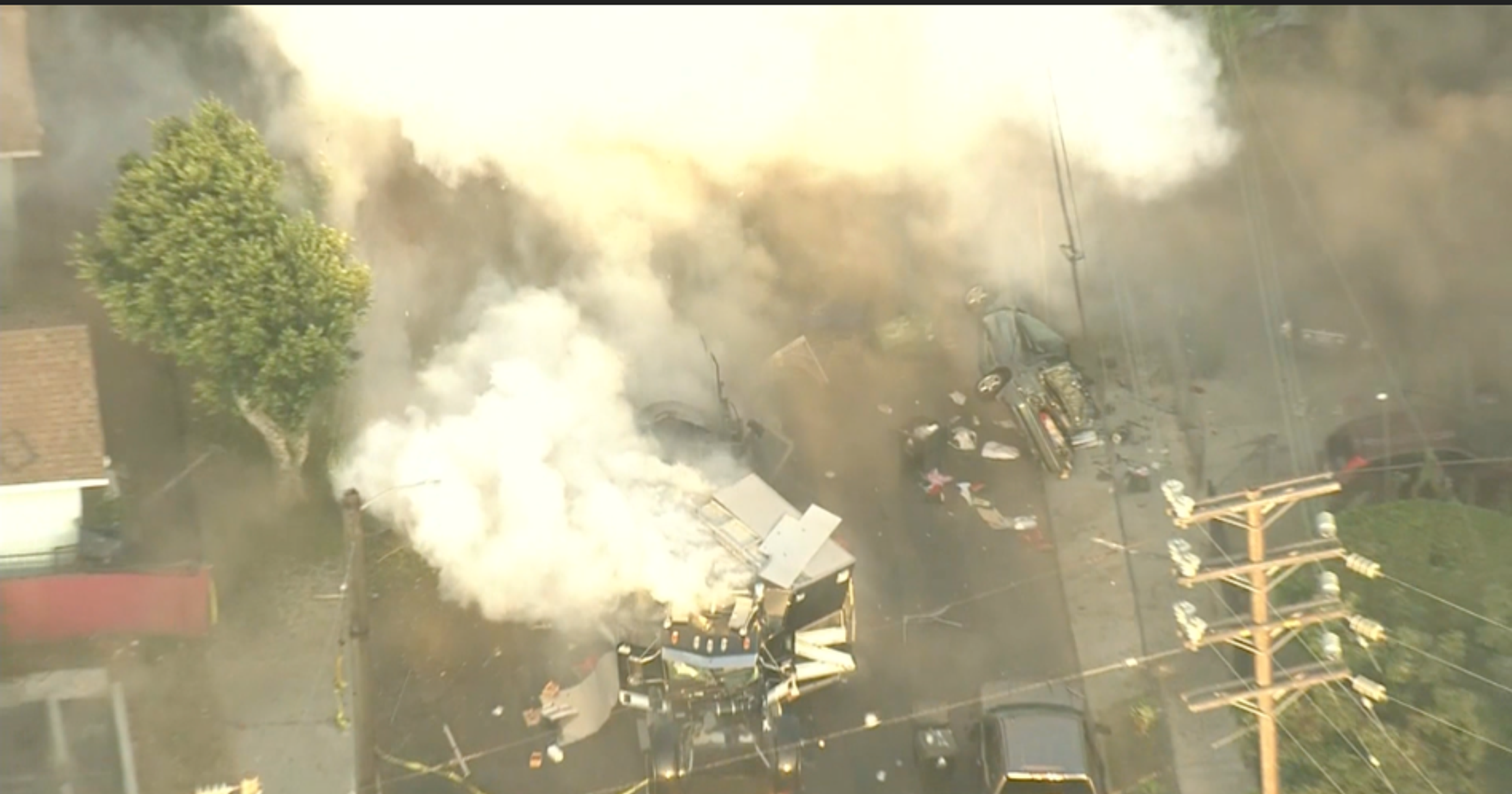 Overhead picture of LAPD fireworks explosion, courtesy CBS News. Shows the exploded containment vessel, an overturned car, a tree, power lines, and copious smoke obscuring the rest of the blast damage.