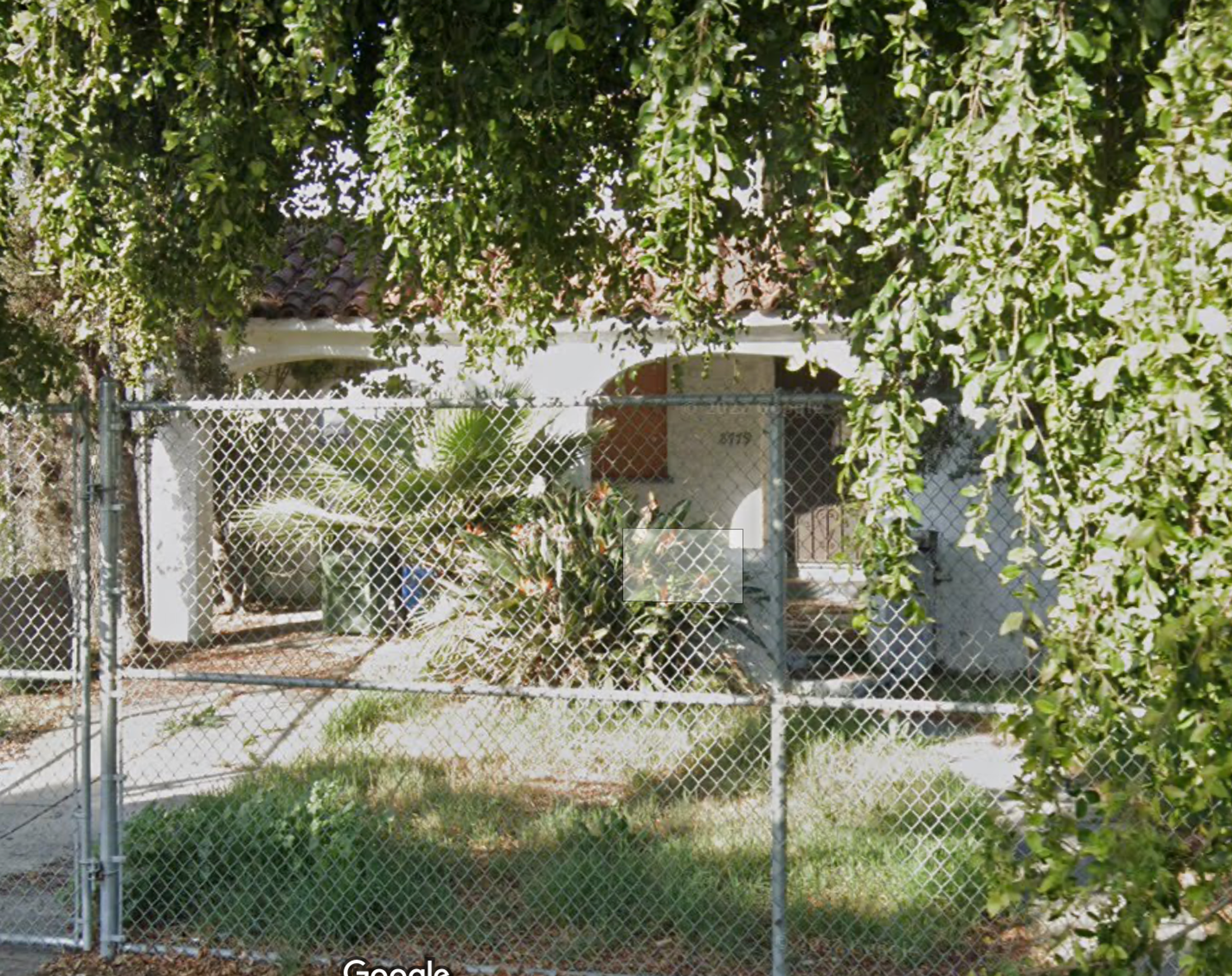 8779 South Hobart Boulevard, a single-story Spanish-style house behind a chain-link fence and on a lot with overgrown vegetation.