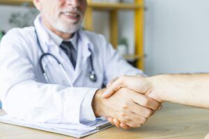 A senior doctor in a white coat with a stethoscope around his neck shakes hand. Symbolizing trust, partnership, and strong relationships in healthcare