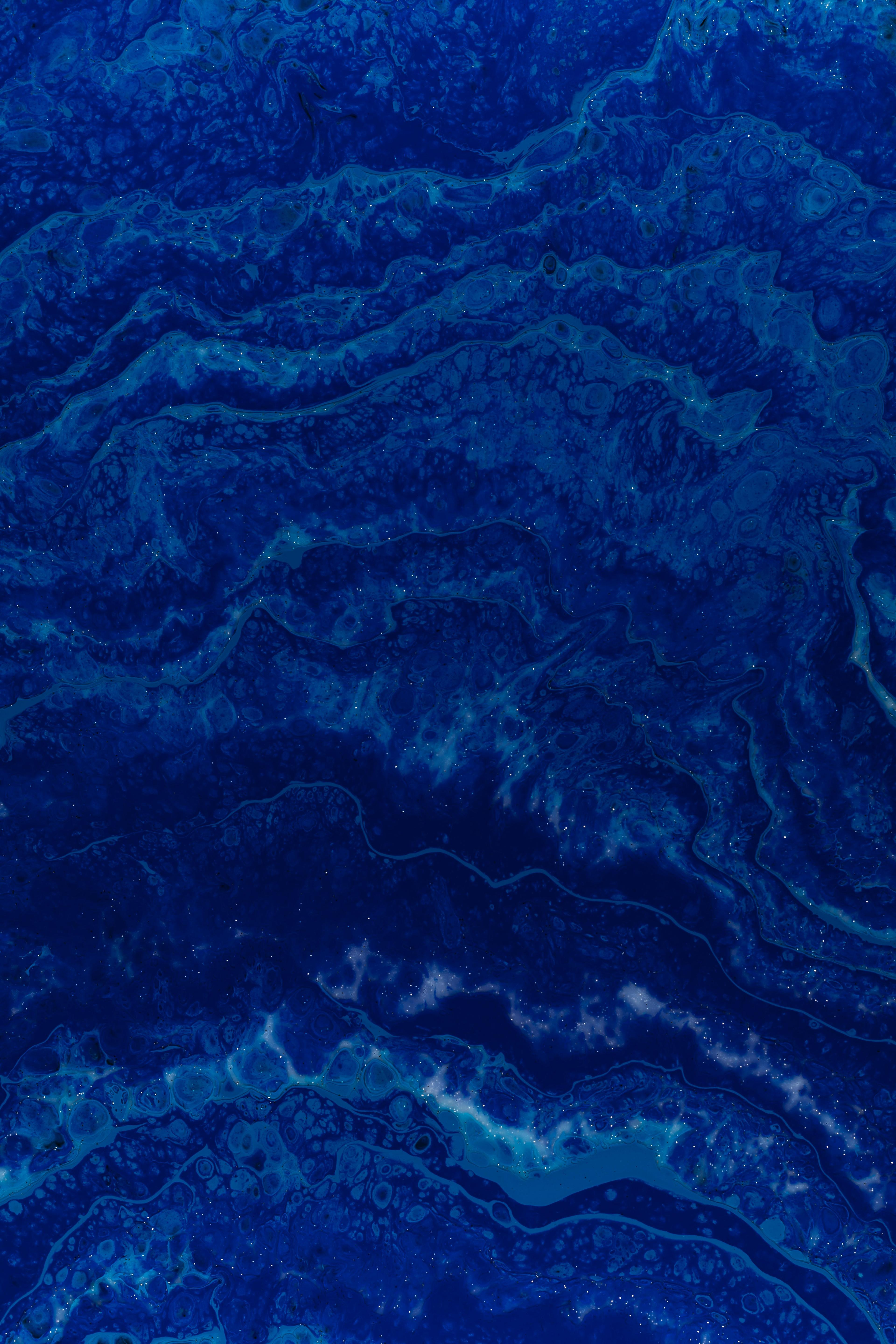 Abstract fluid-paint texture in layered shades of deep blue resembling marbled waves with fine speckles.