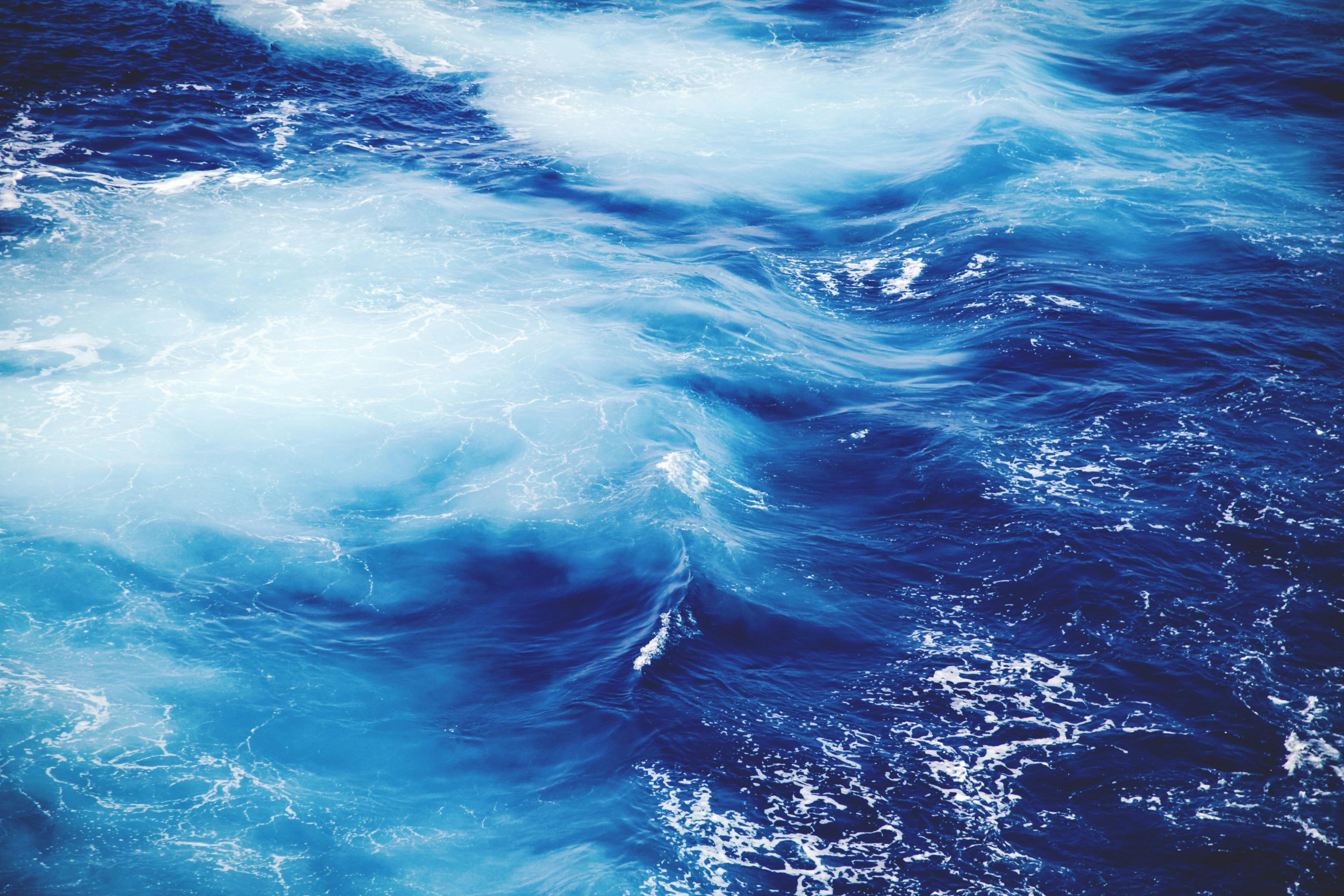 Churning deep blue ocean waves streaked with white foam, seen from above.