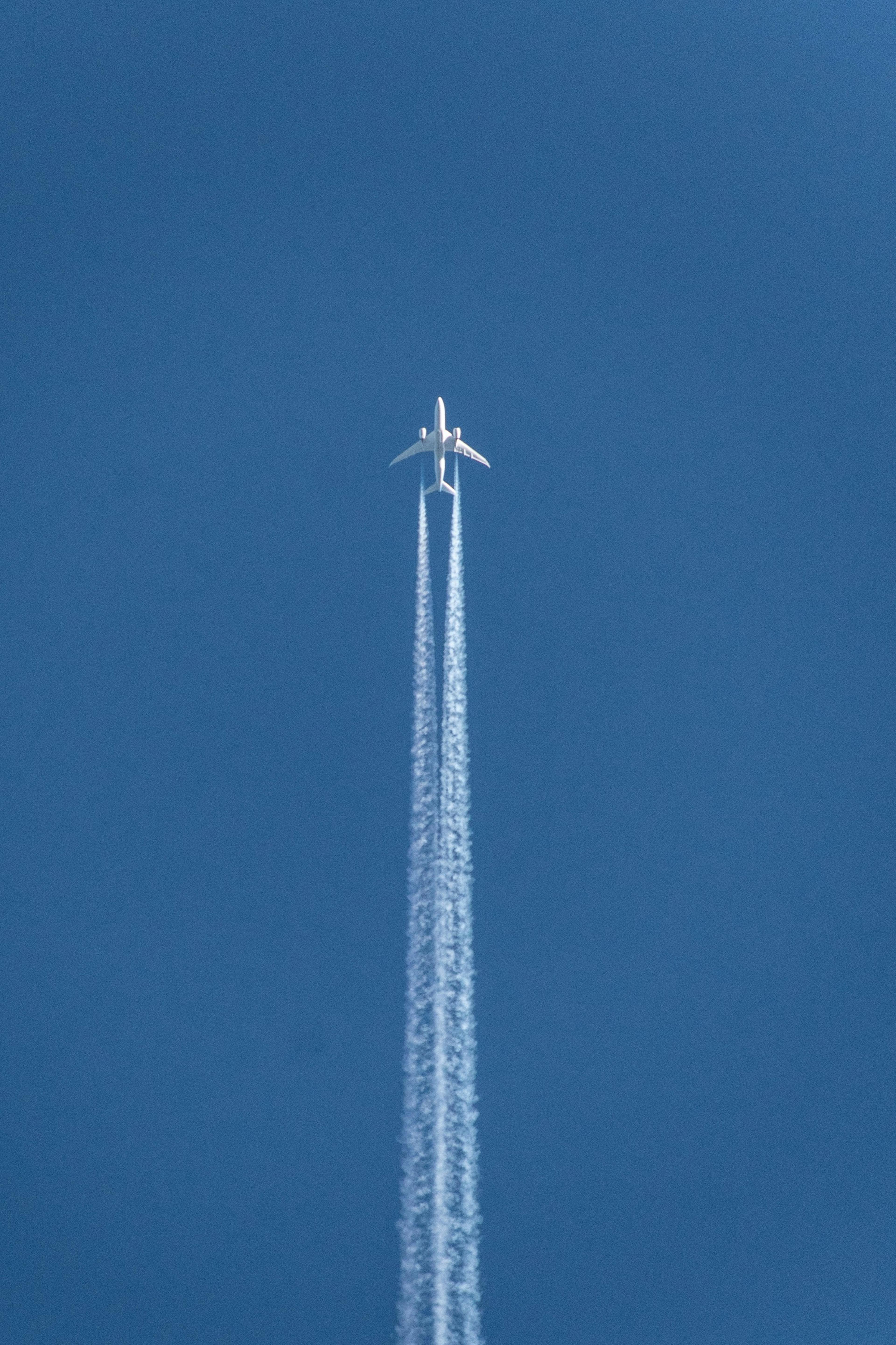 A jet airliner seen from directly below crosses a clear blue sky trailing two white contrails.