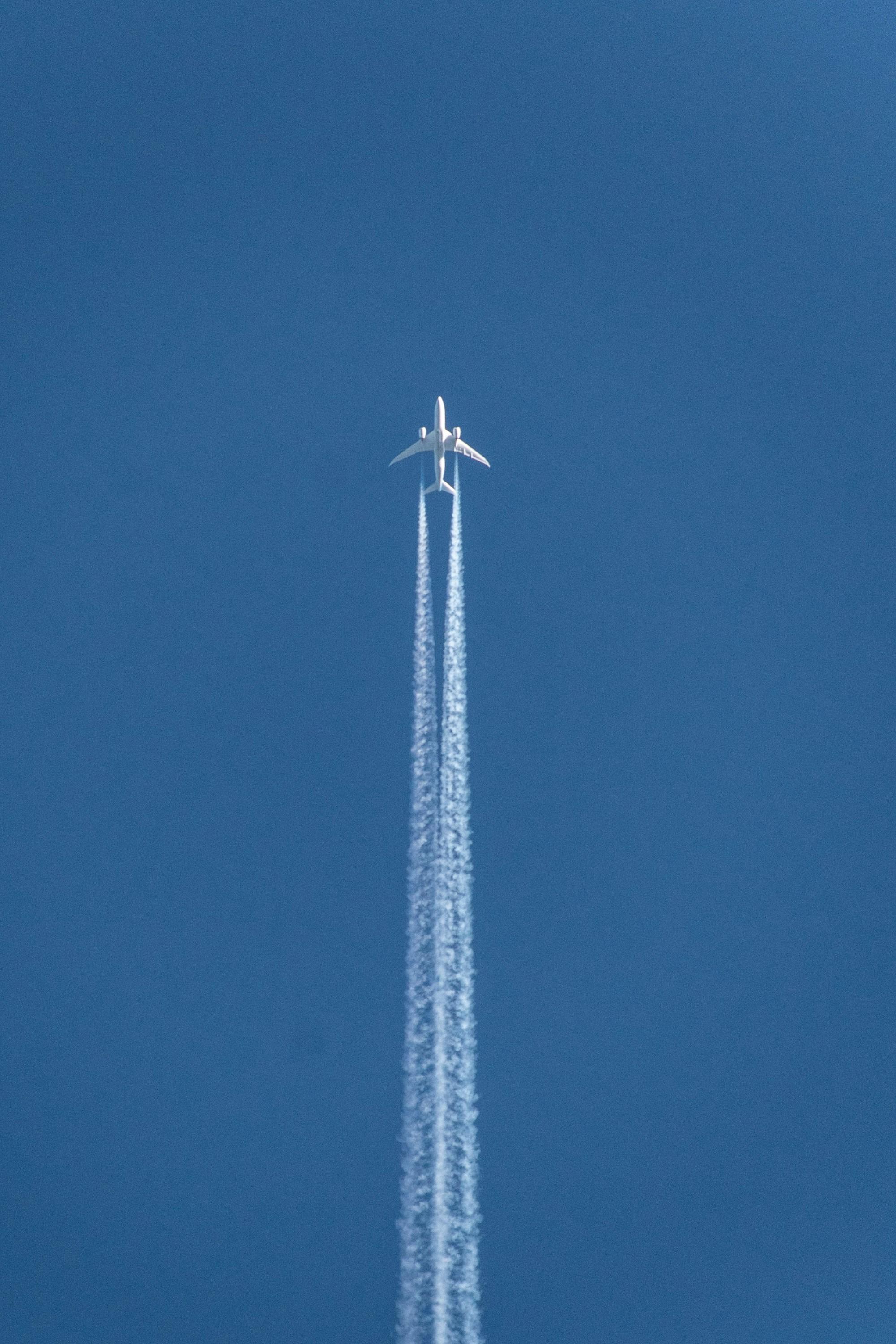 A jet airliner seen from directly below crosses a clear blue sky trailing two white contrails.