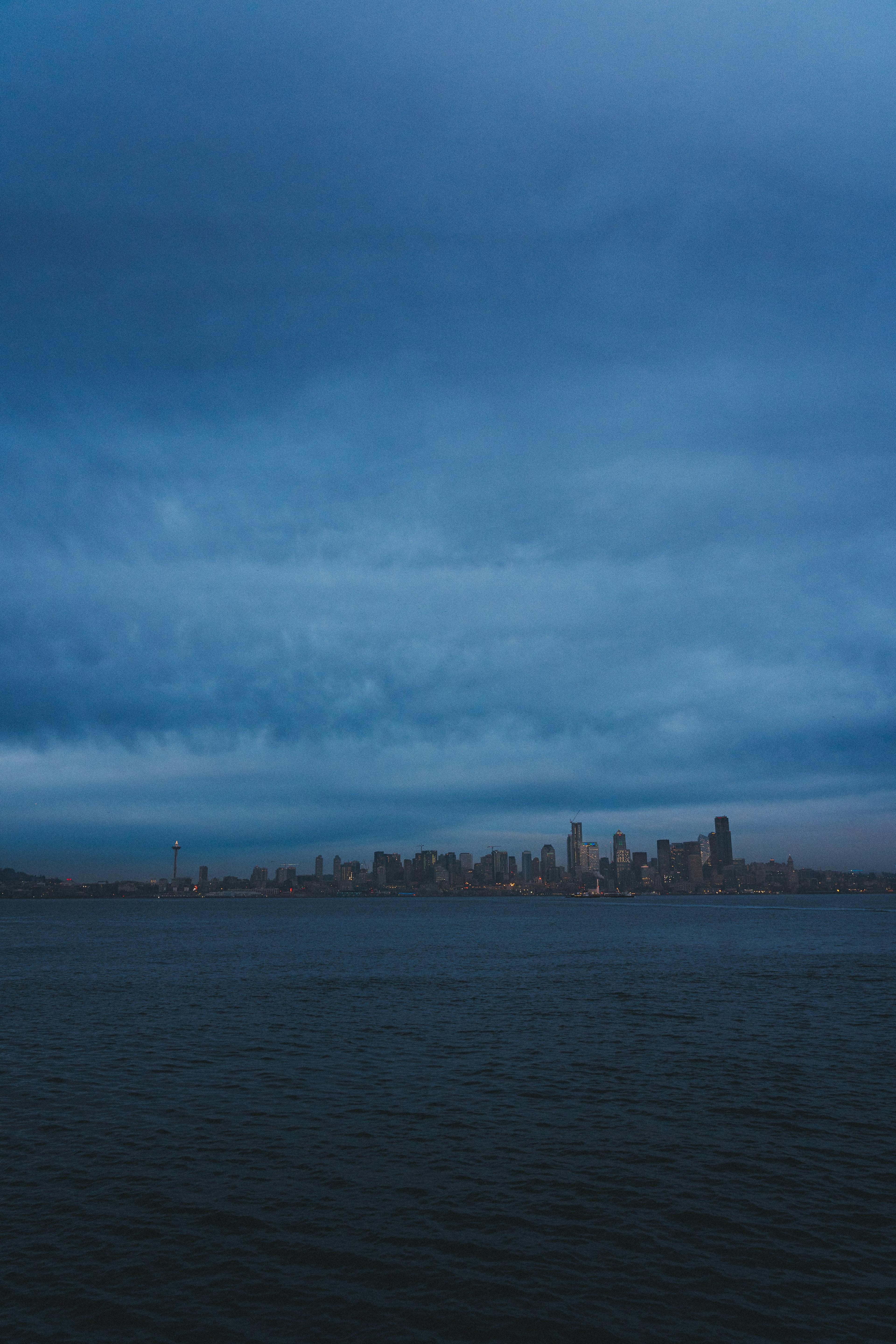 The Seattle skyline with the Space Needle seen across dark water under heavy blue-grey clouds at dusk.