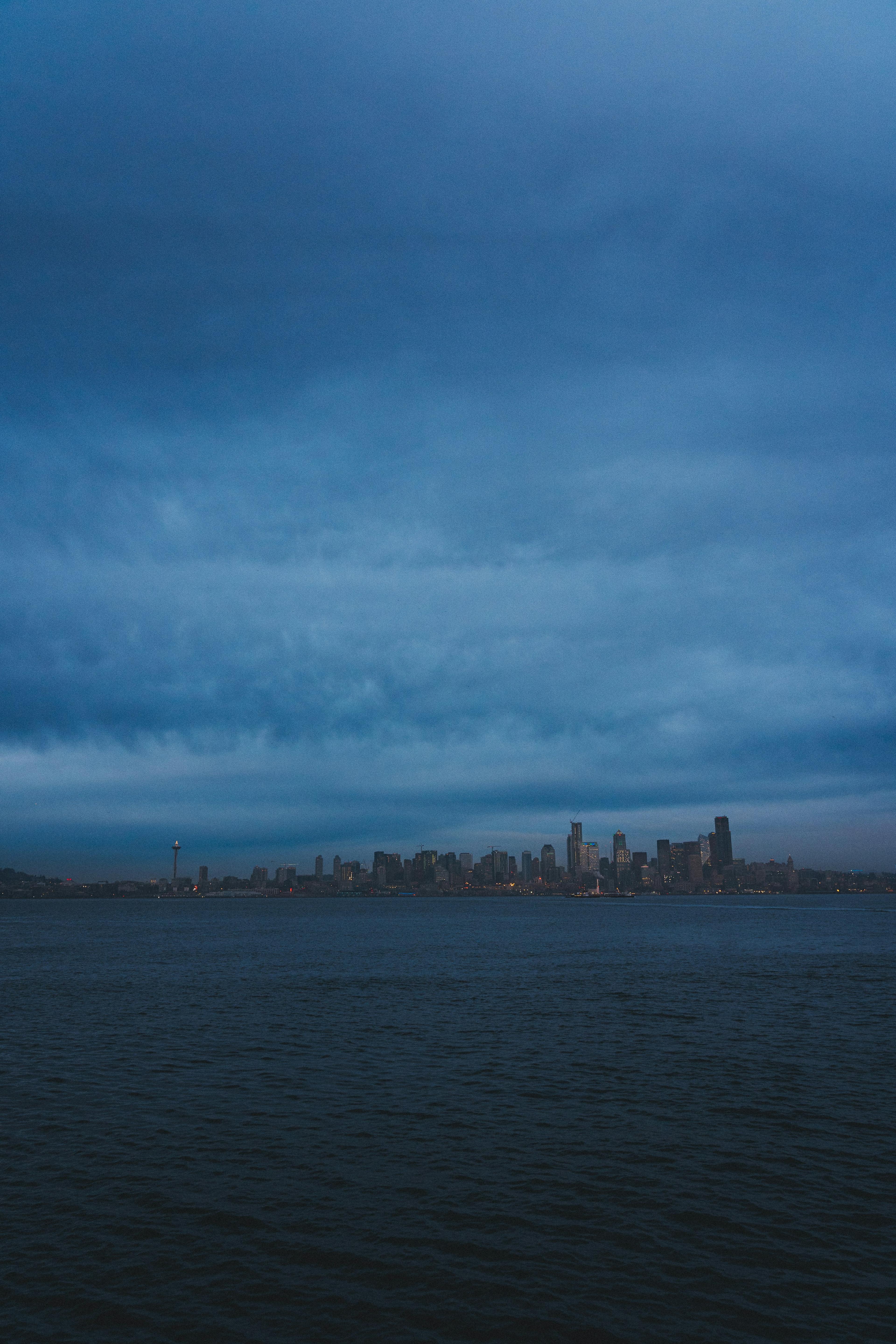The Seattle skyline with the Space Needle seen across dark water under heavy blue-grey clouds at dusk.