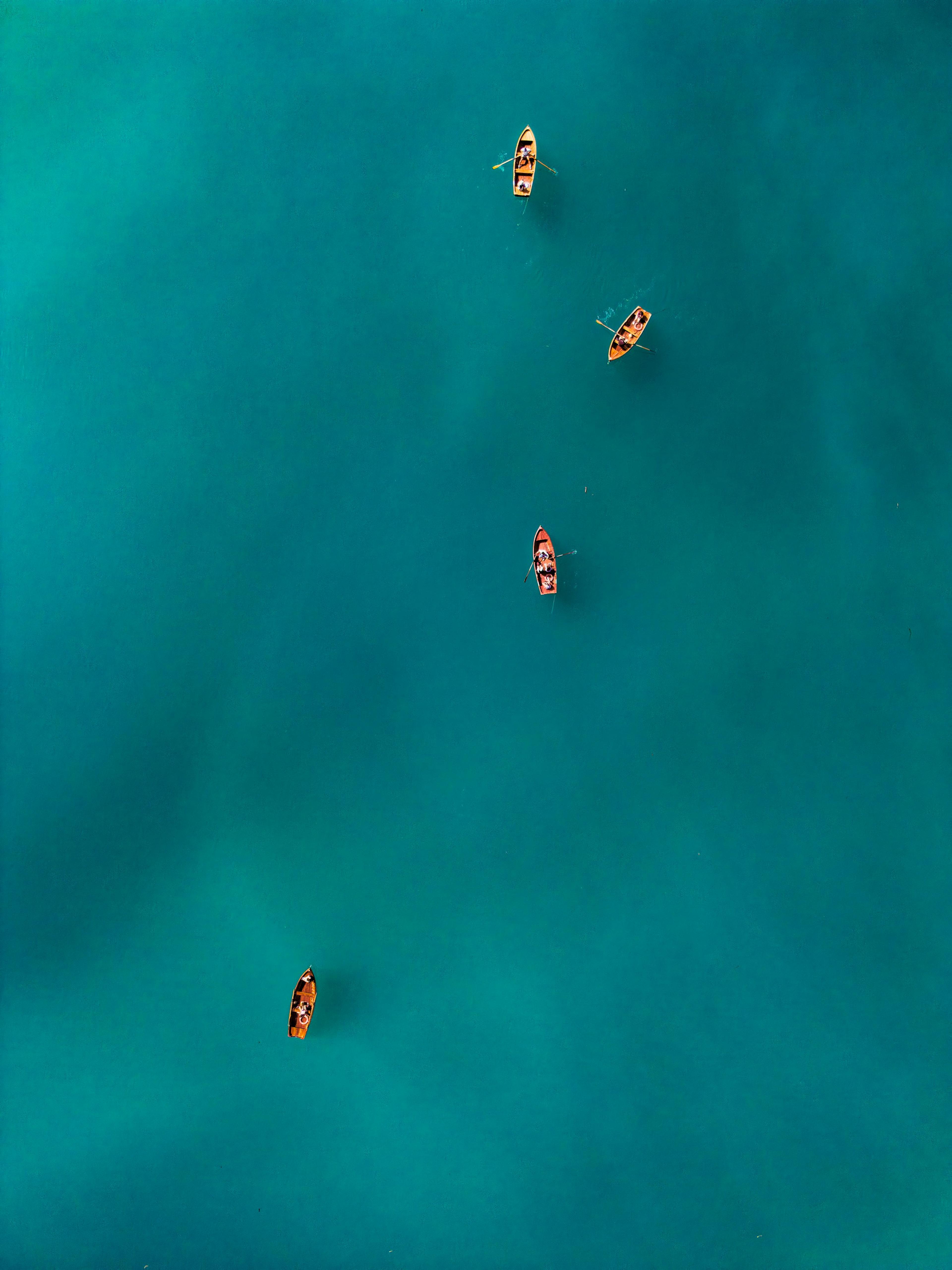 Aerial view of four small wooden rowboats scattered across calm teal water.
