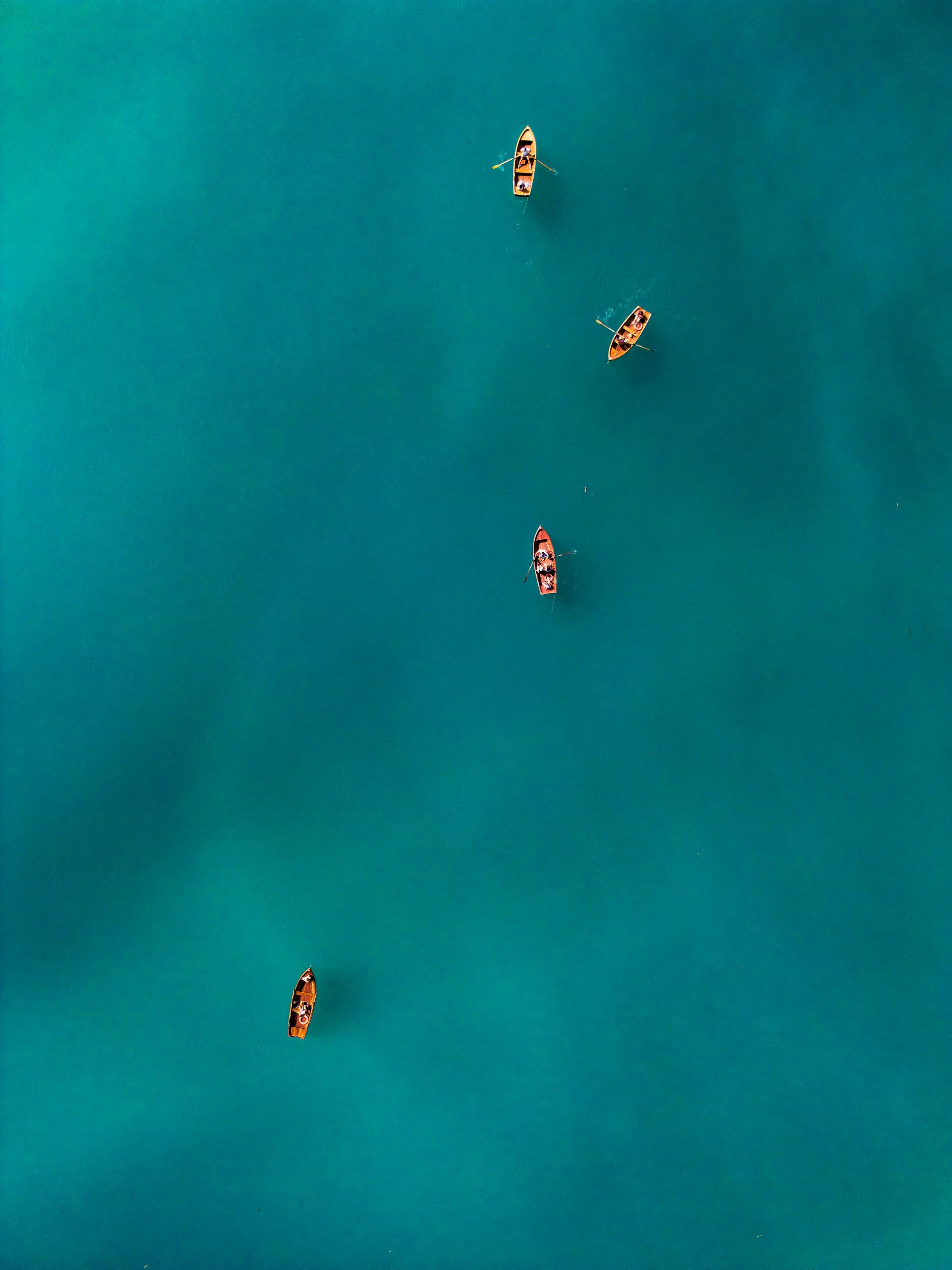 Aerial view of four small wooden rowboats scattered across calm teal water.