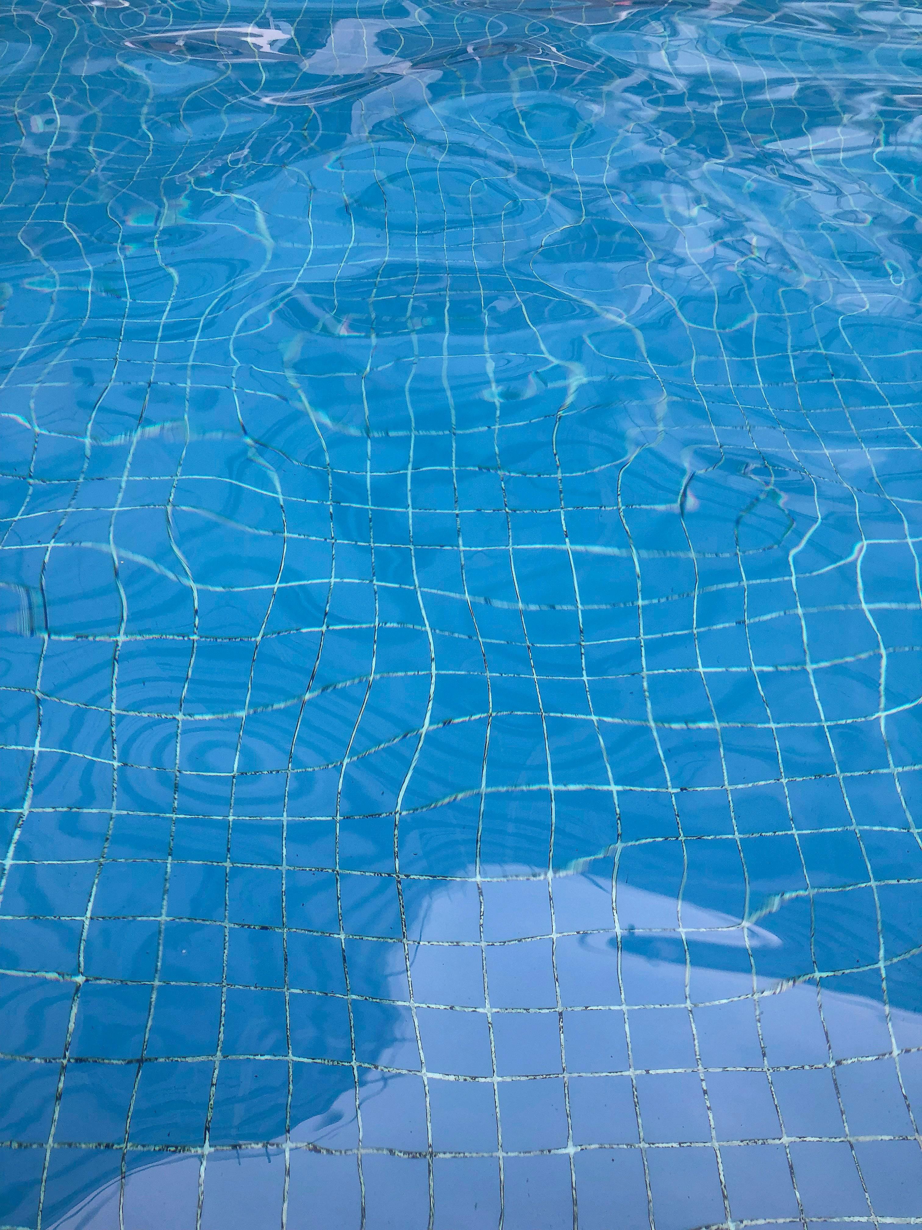 Rippling water in a tiled swimming pool distorts the grid of square blue tiles below.