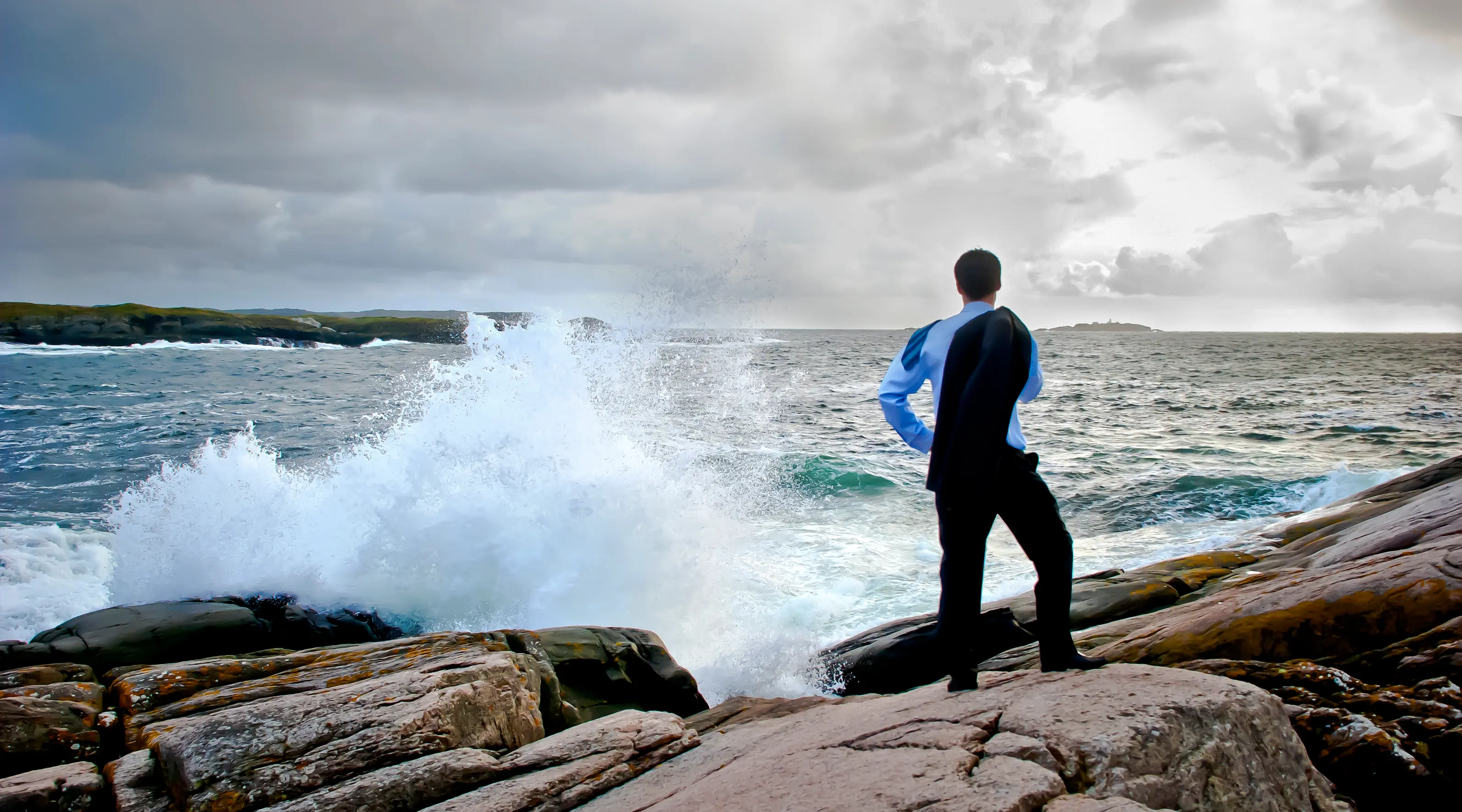 A guy in a suit facing the brutal waves of the ocean from the shore