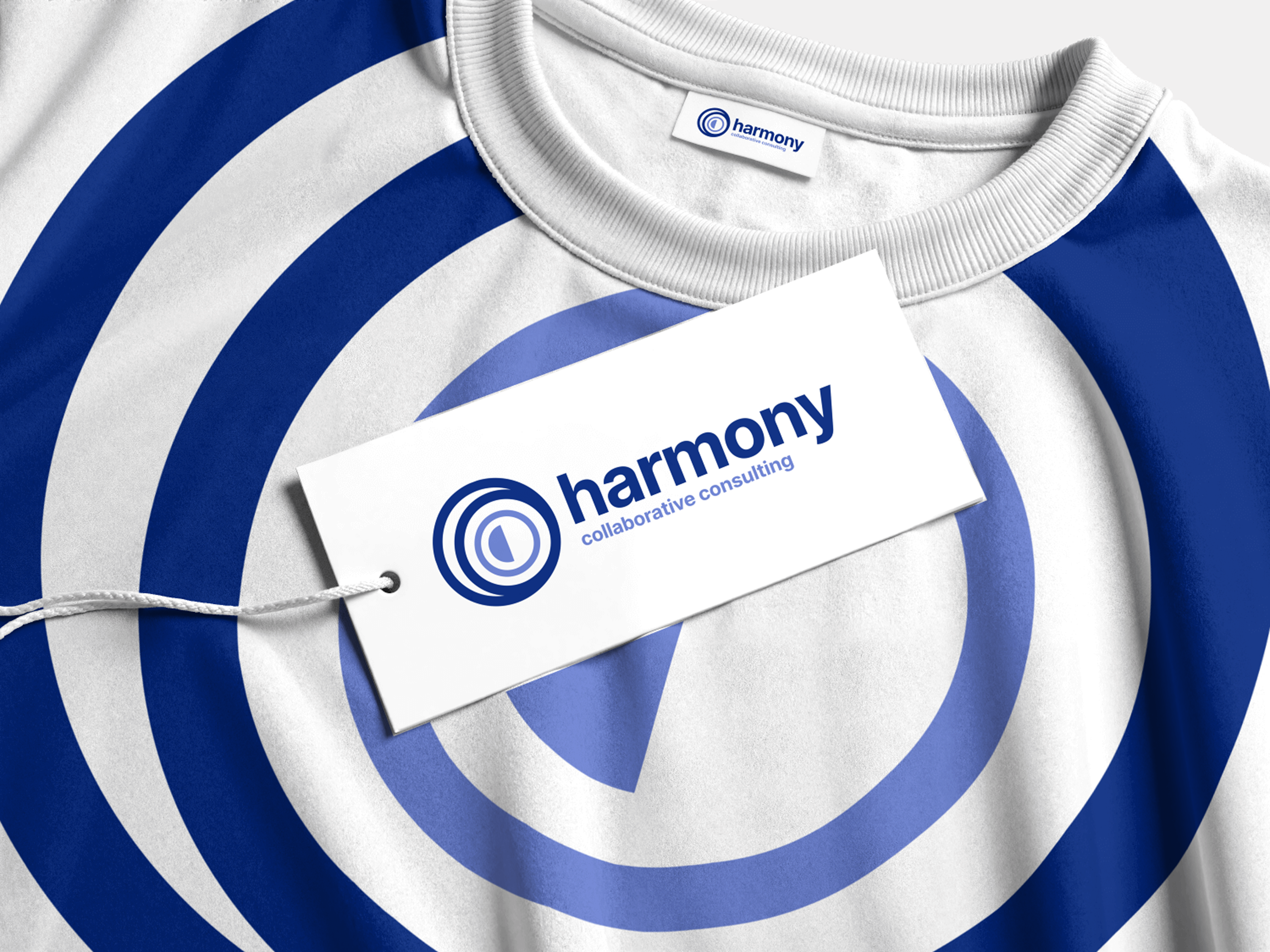 White t-shirt with blue concentric circles, featuring a Harmony collaborative consulting hang tag and a Harmony collar label.