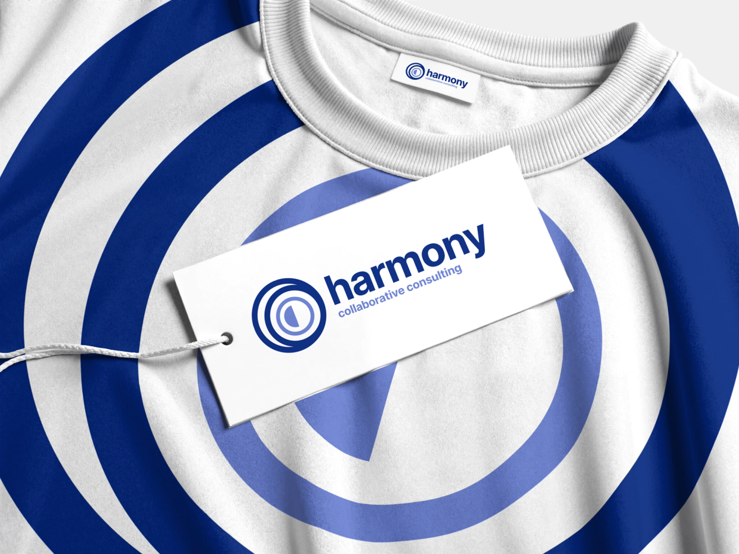 White t-shirt with blue concentric circles, featuring a Harmony collaborative consulting hang tag and a Harmony collar label.