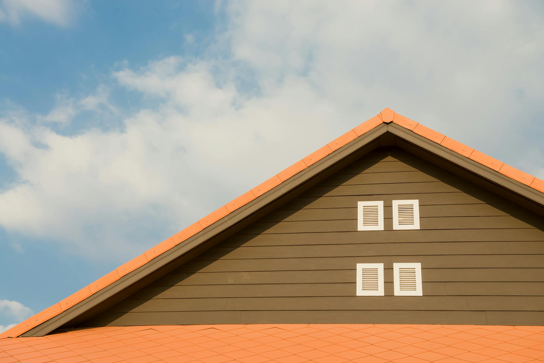 Modern house facade featuring orange roof and shuttered windows against a bright blue sky.