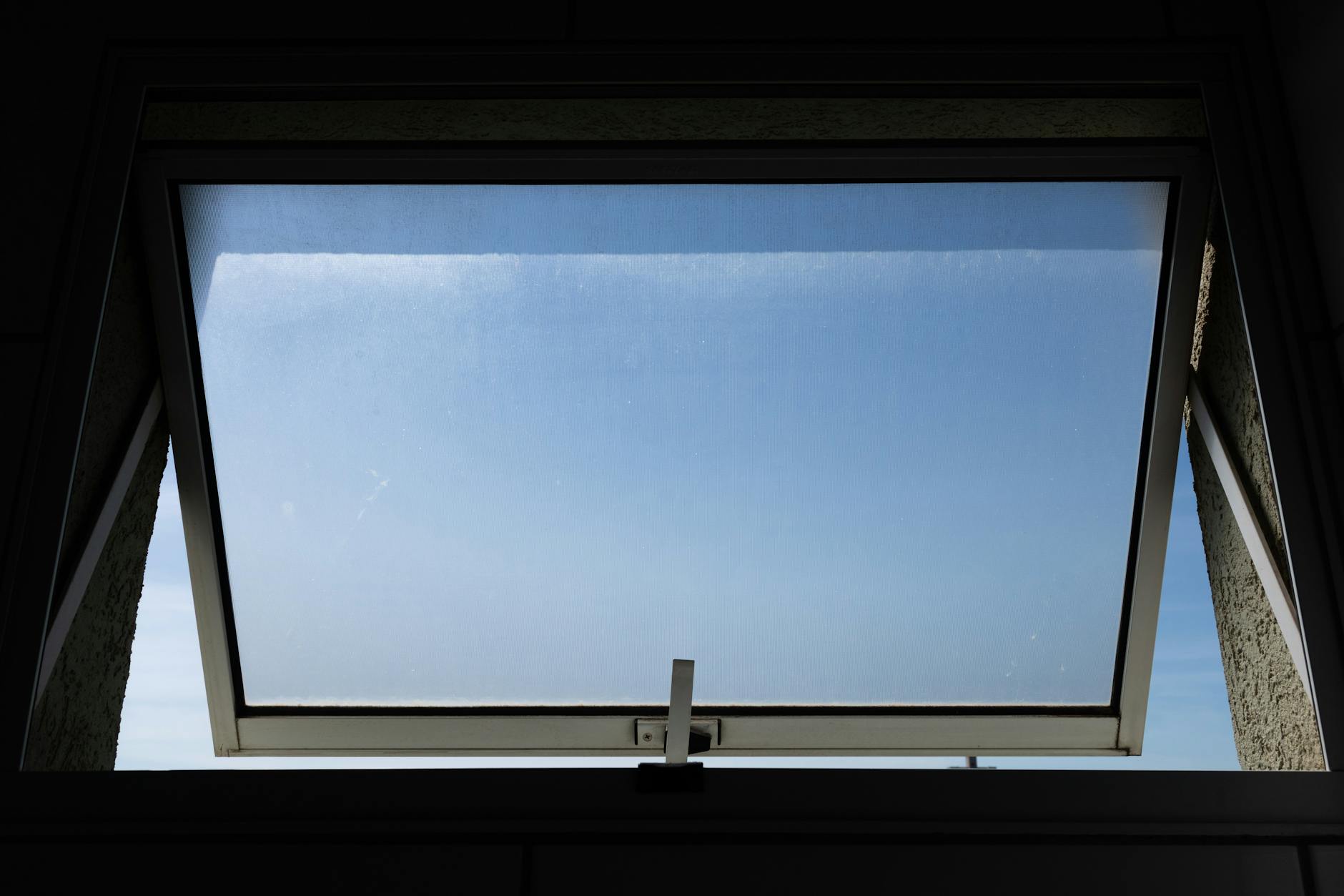 A low angle view of an open skylight window revealing a clear blue sky.