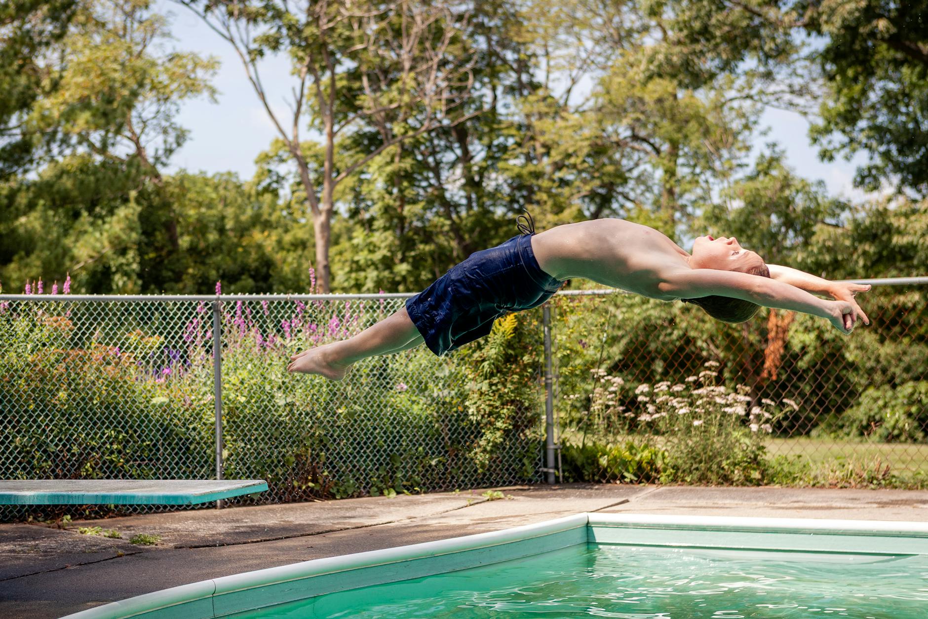 A young boy gracefully dives into a backyard swimming pool on a bright summer day.