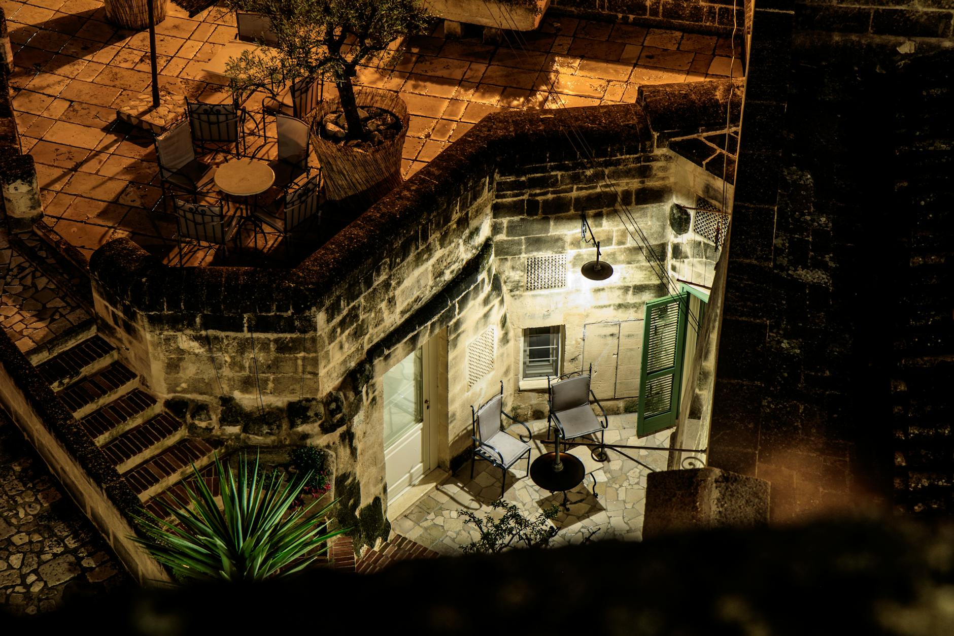 Aerial view of a cozy illuminated courtyard with furniture in Basilicata, Italy at night.