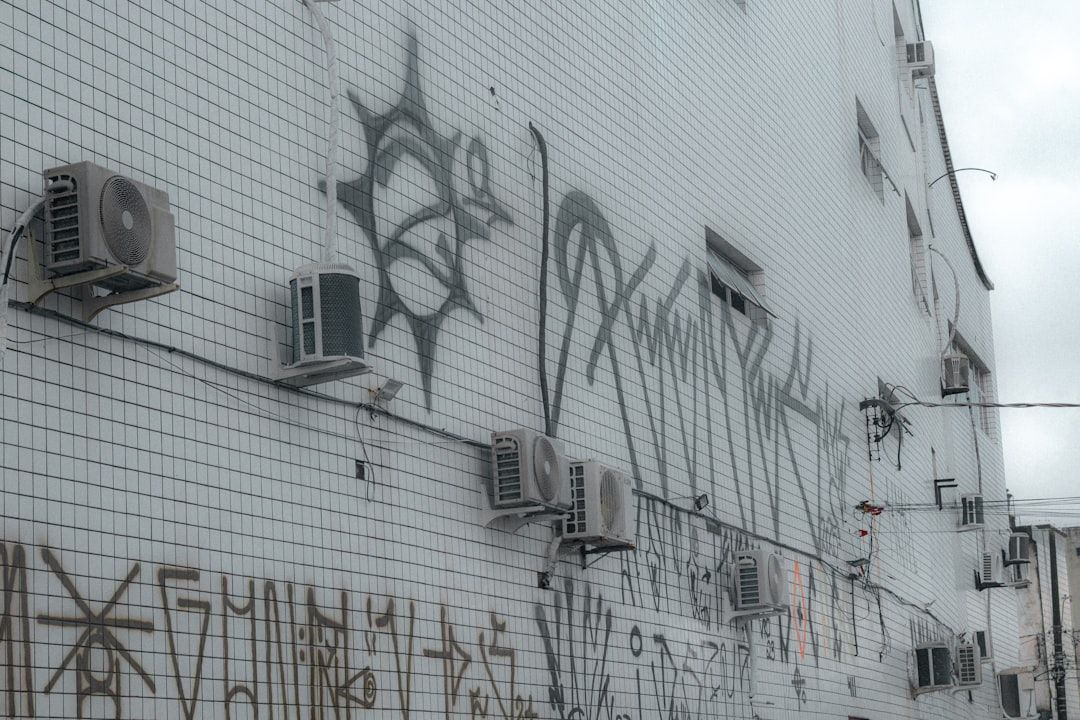 Graffiti covers a tiled building wall with air conditioners.