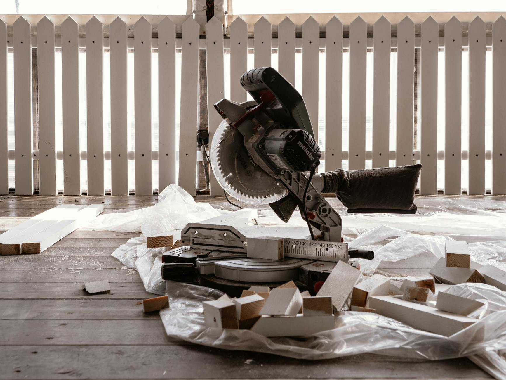 A circular saw on a wooden terrace with cut wood pieces and a white fence.