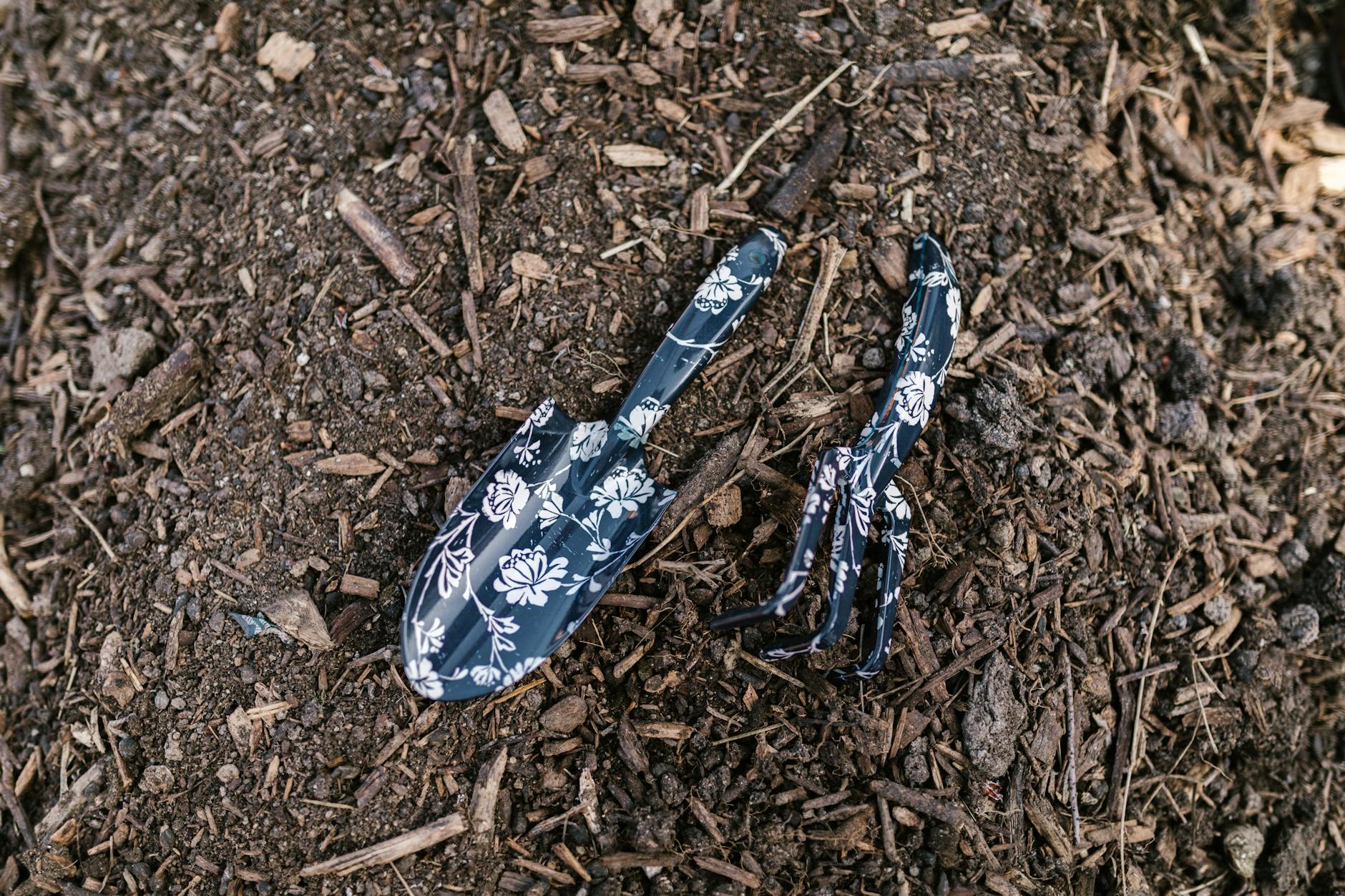 Close-up of floral patterned rake and shovel resting on soil, ideal for gardening themes.