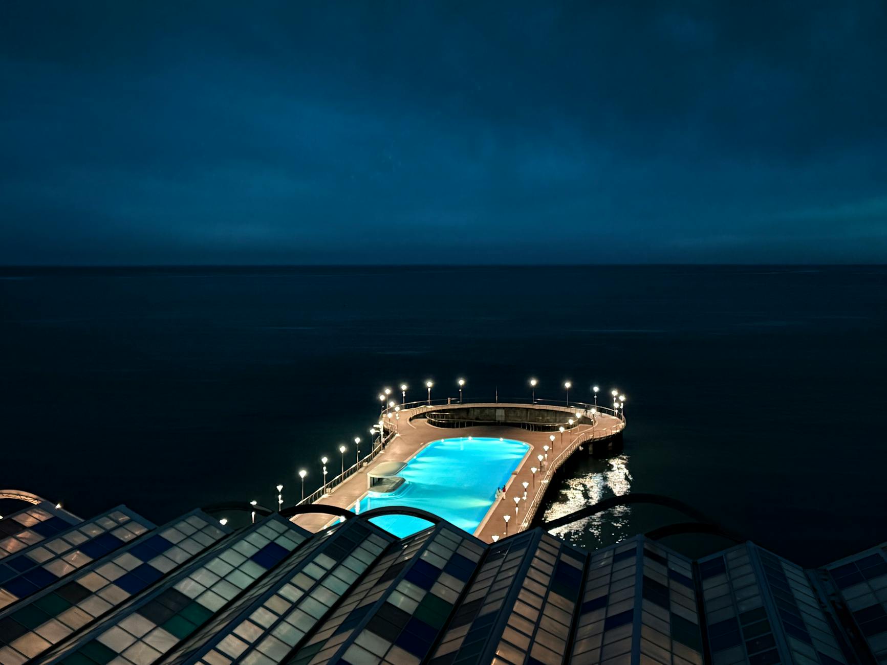 Stunning view of illuminated coastal swimming pool by the sea at twilight.