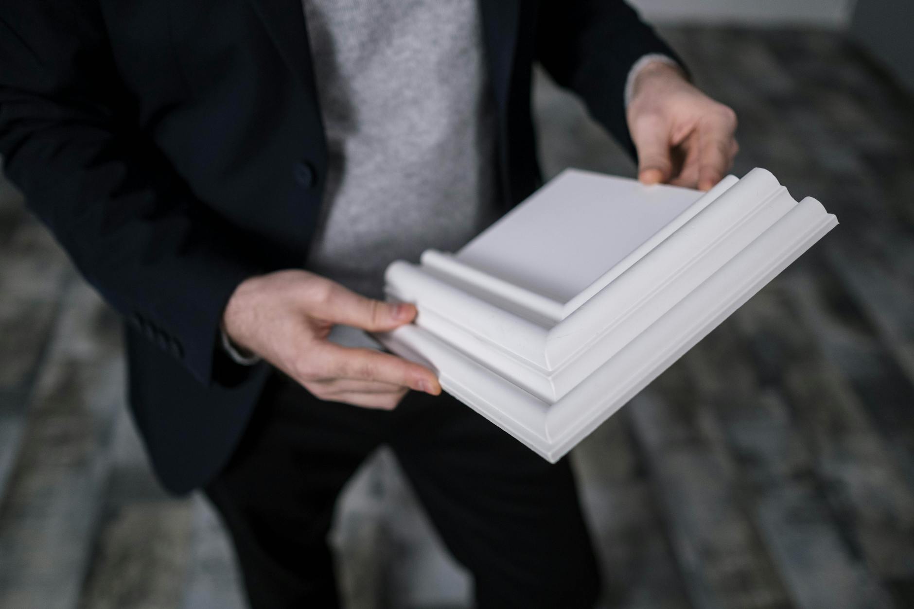 Close-up of a person holding a white crown molding sample indoors.