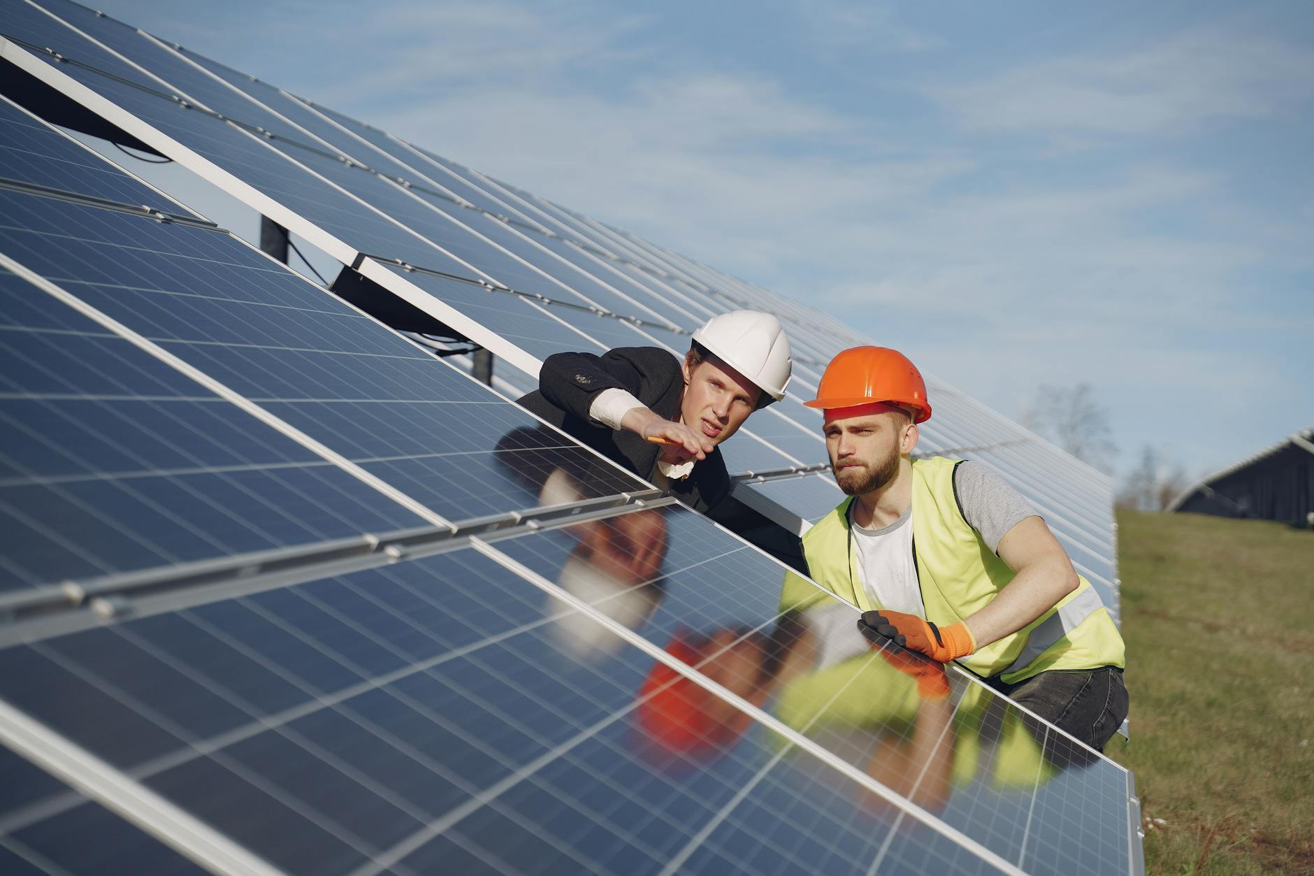 Concentrated male coworkers in hardhats working at solar energy station and discussing technical aspects of panels