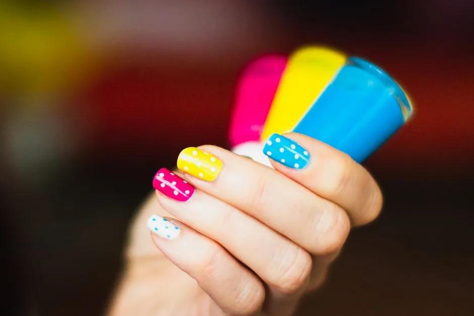Hand med färgglada polka dot sommarnaglar 2026 håller nagellacksflaskor