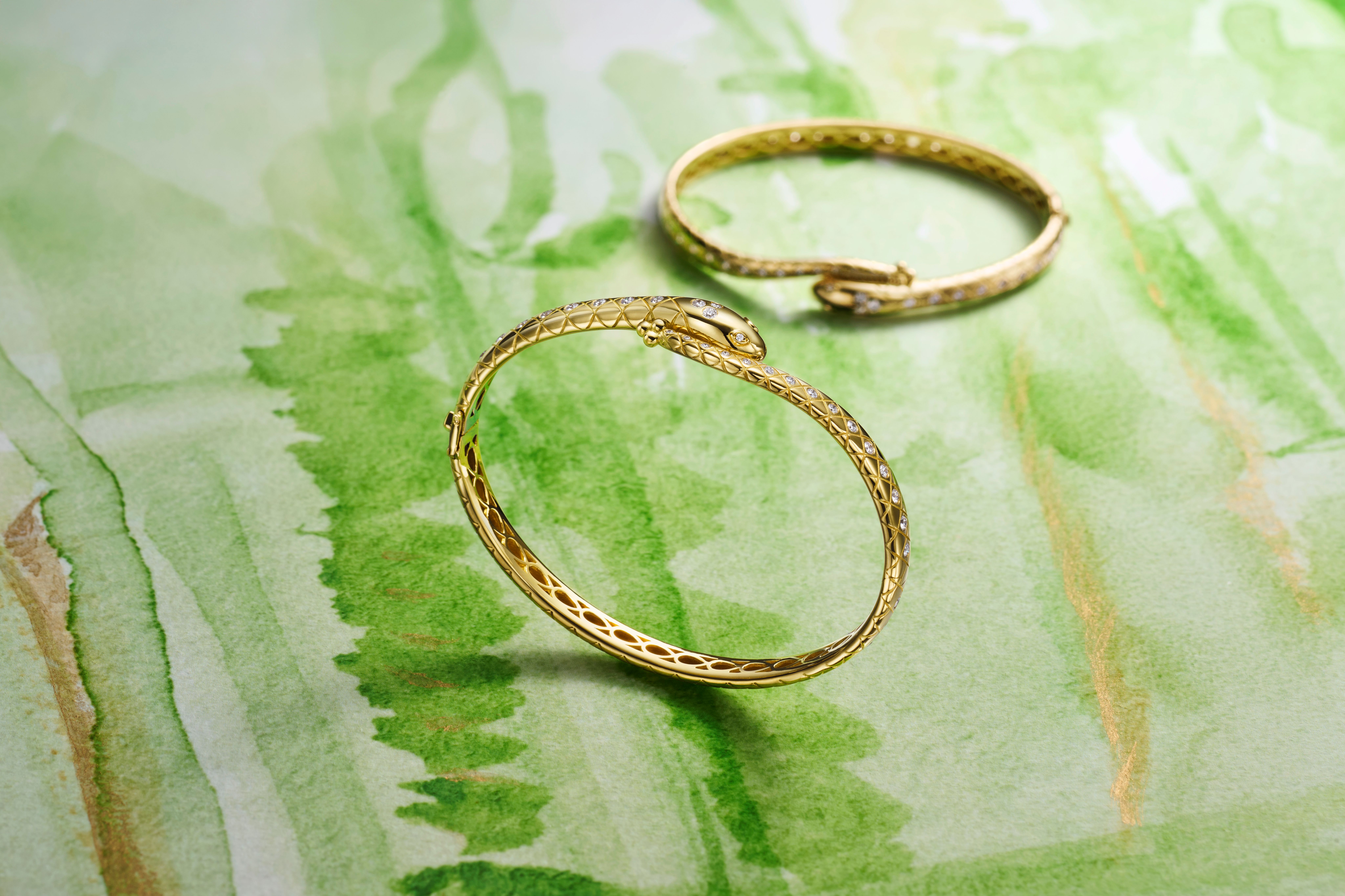 Two gold snake bracelets adorned with diamonds on a green watercolor background.