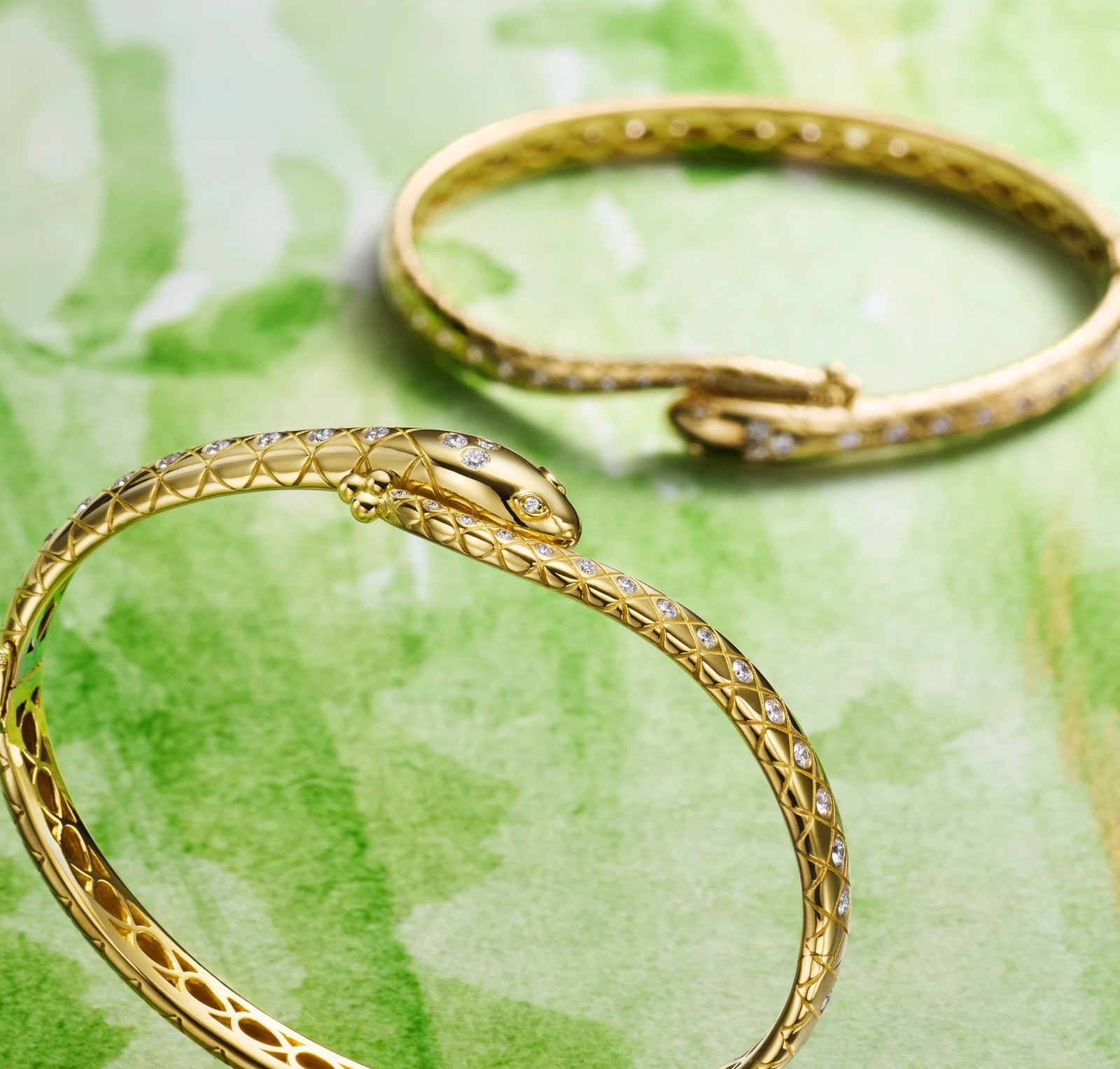 Two gold snake bracelets adorned with diamonds on a green watercolor background.
