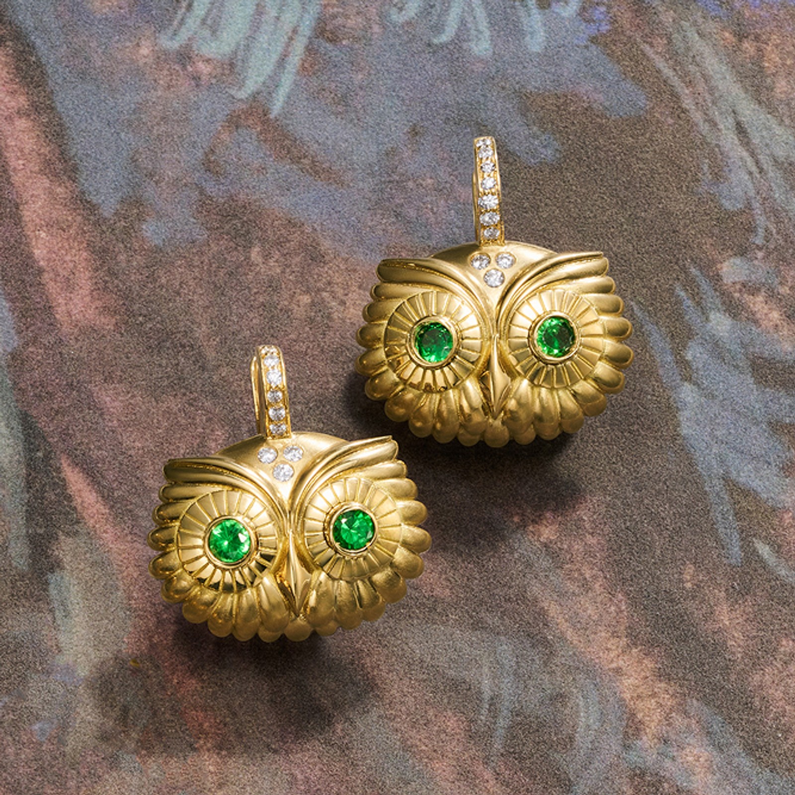 Two gold owl earrings with emerald eyes and diamond accents.