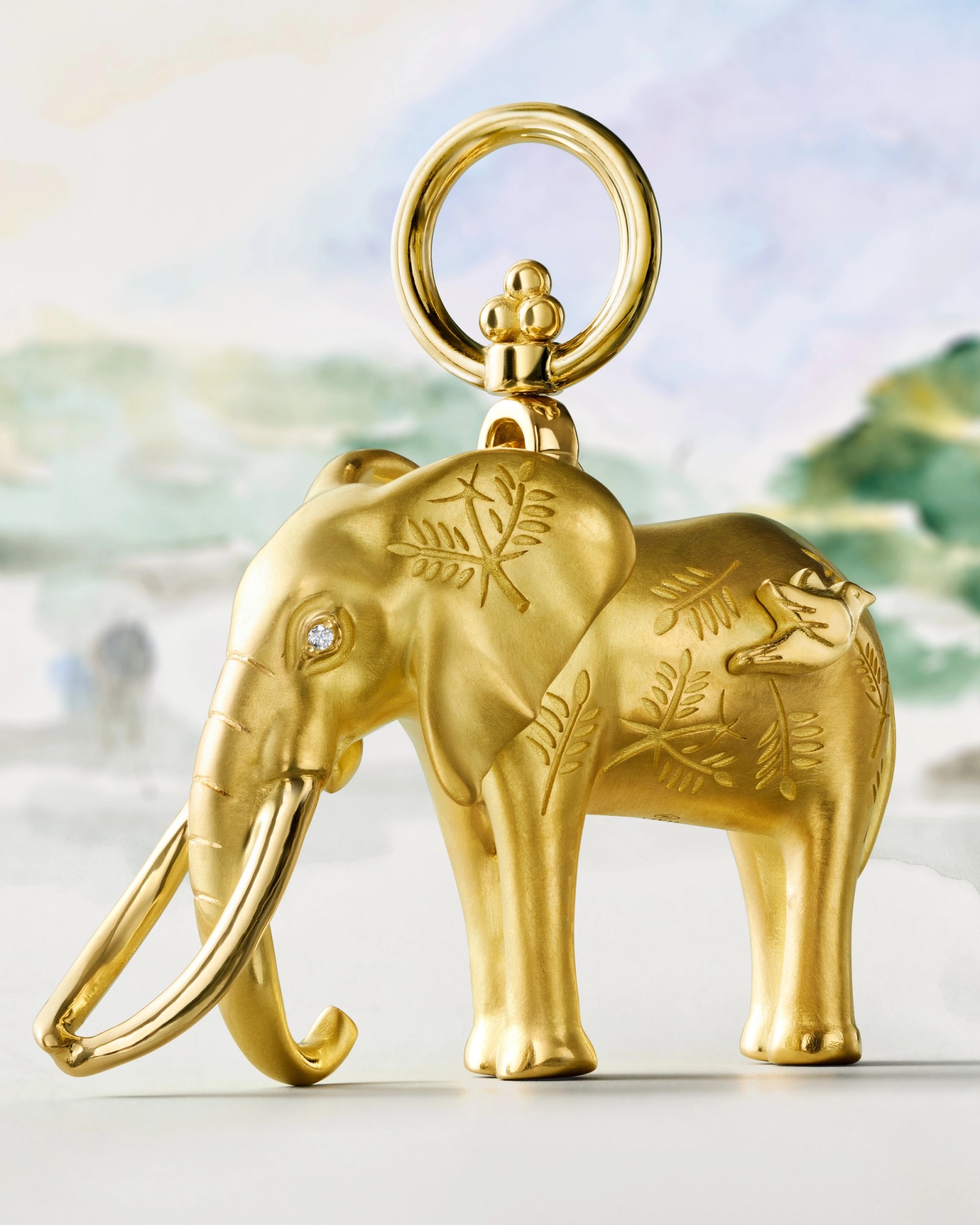 Golden elephant charm with engraved leaves, a diamond eye, and a hanging loop.