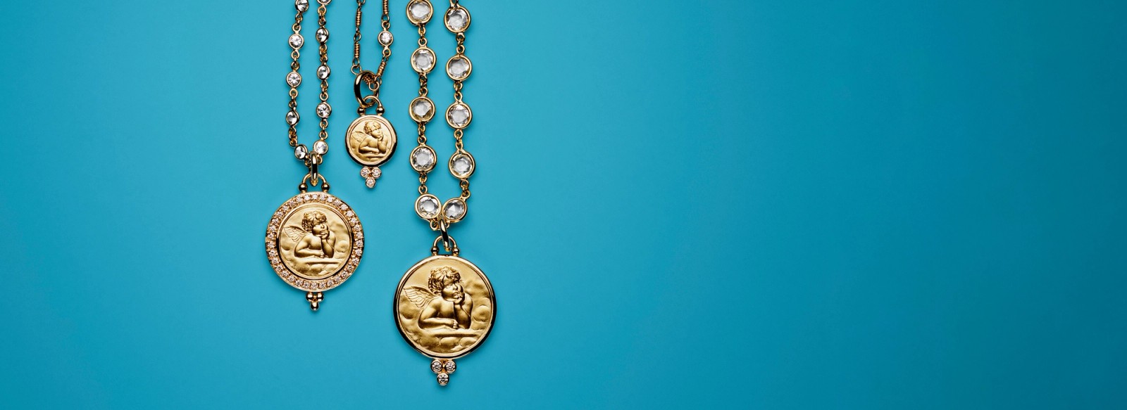 Two gold necklaces with cherub medallions and clear stones on a teal background.