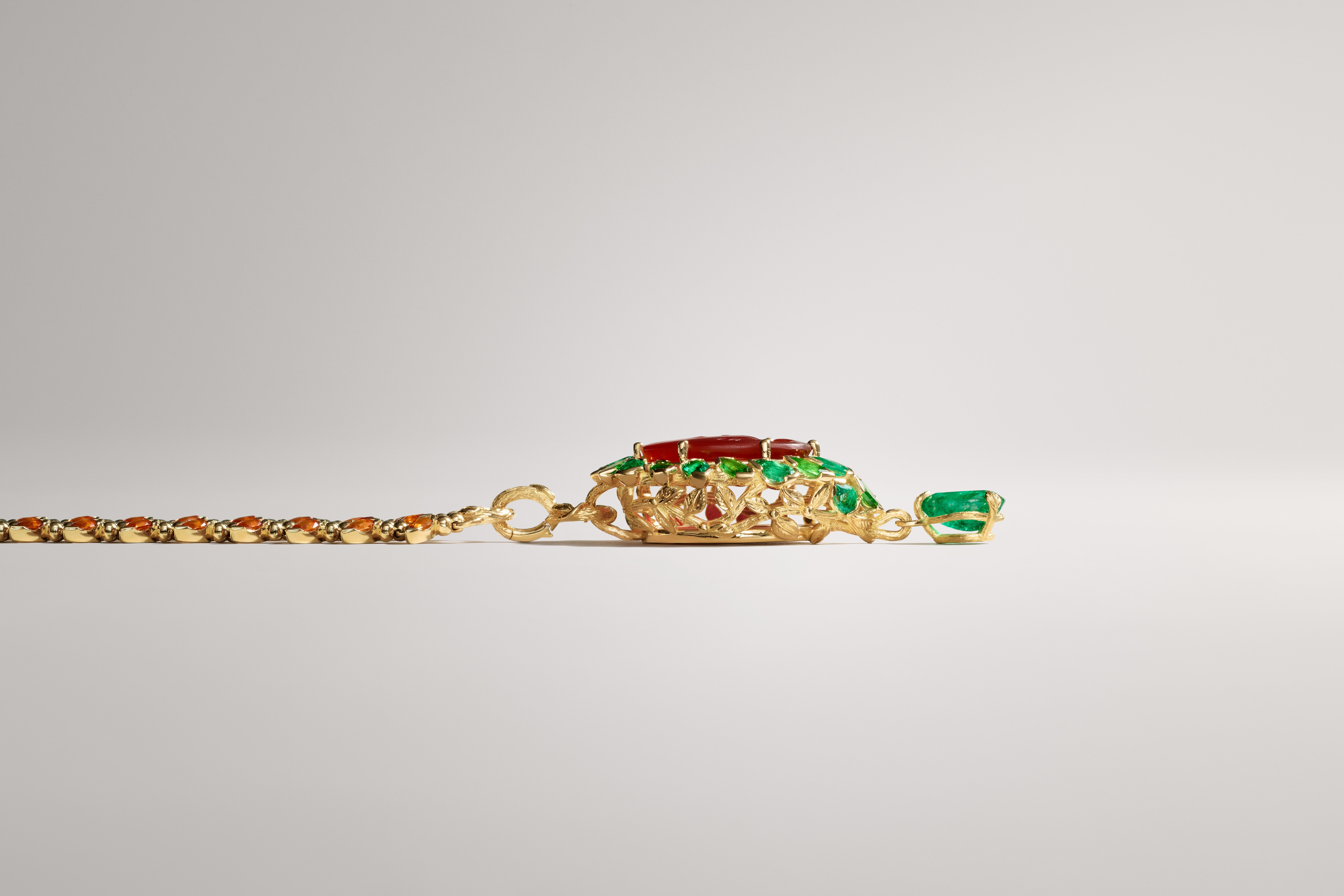 Gold jewelry with a pendant featuring red and green gemstones, attached to a chain with small orange stones.