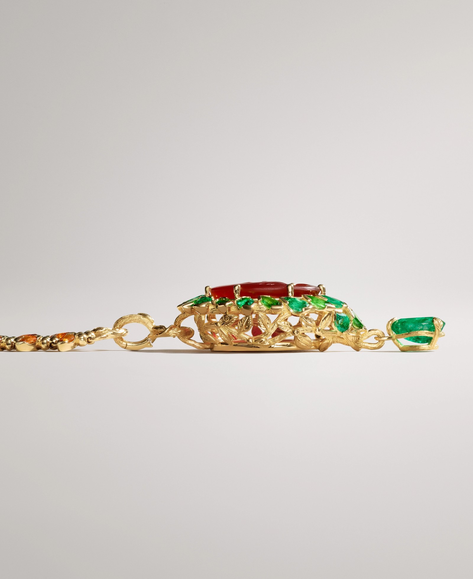 Gold jewelry with a pendant featuring red and green gemstones, attached to a chain with small orange stones.