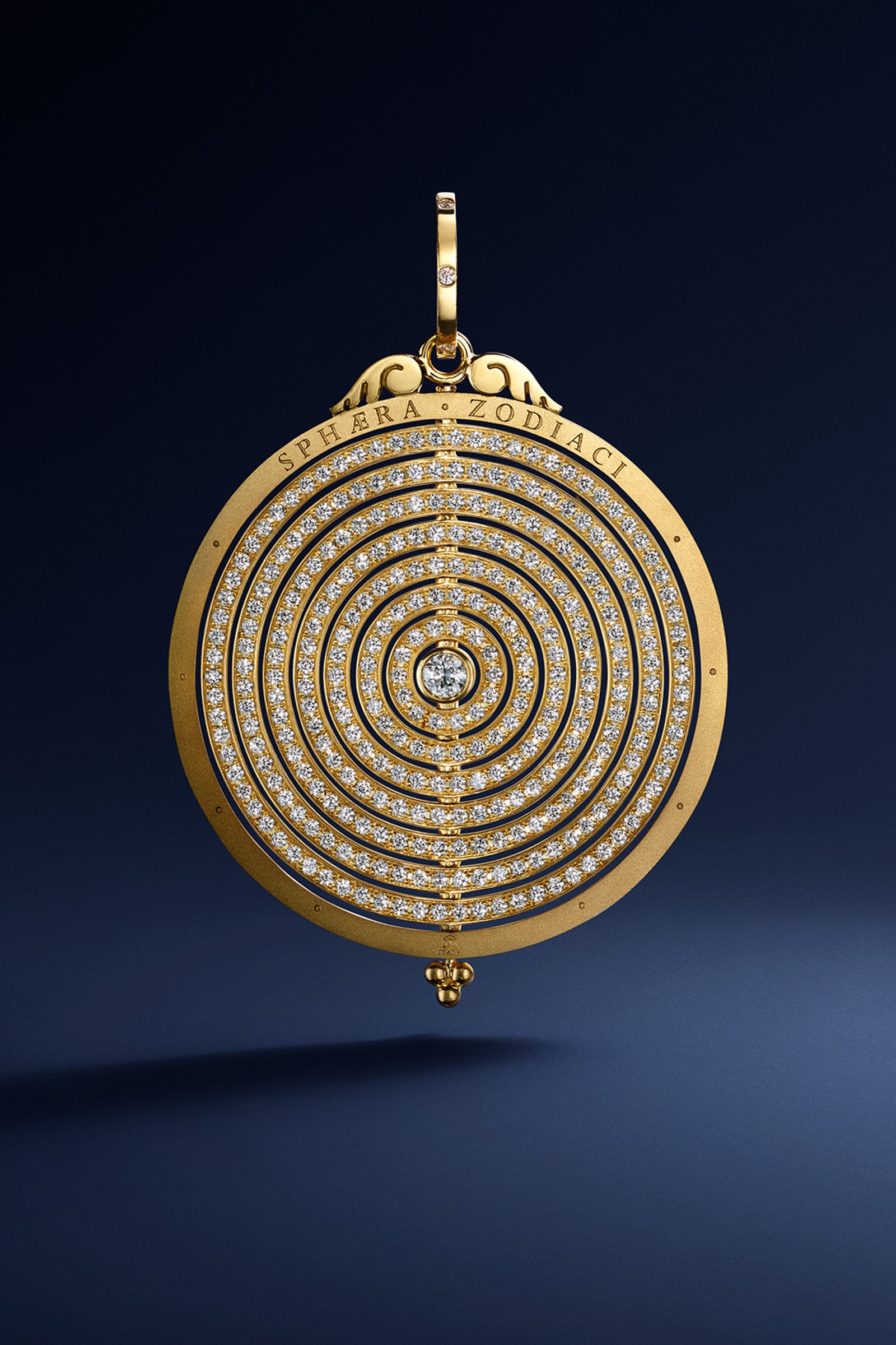 A gold circular pendant with concentric rings paved with diamonds, a central diamond, and "SPHERA ZODIAC" inscribed at the top.