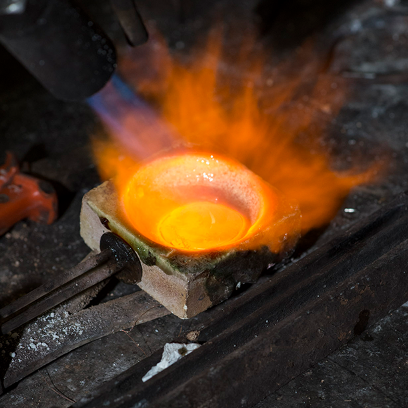 A torch heats glowing molten metal in a crucible.