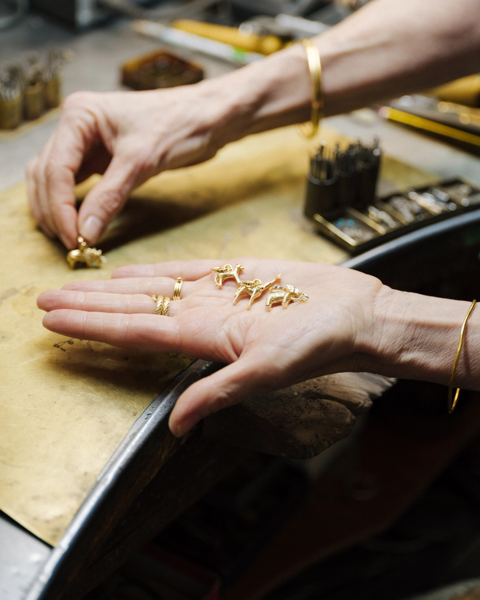 Hands selecting small gold animal charms at a workbench.