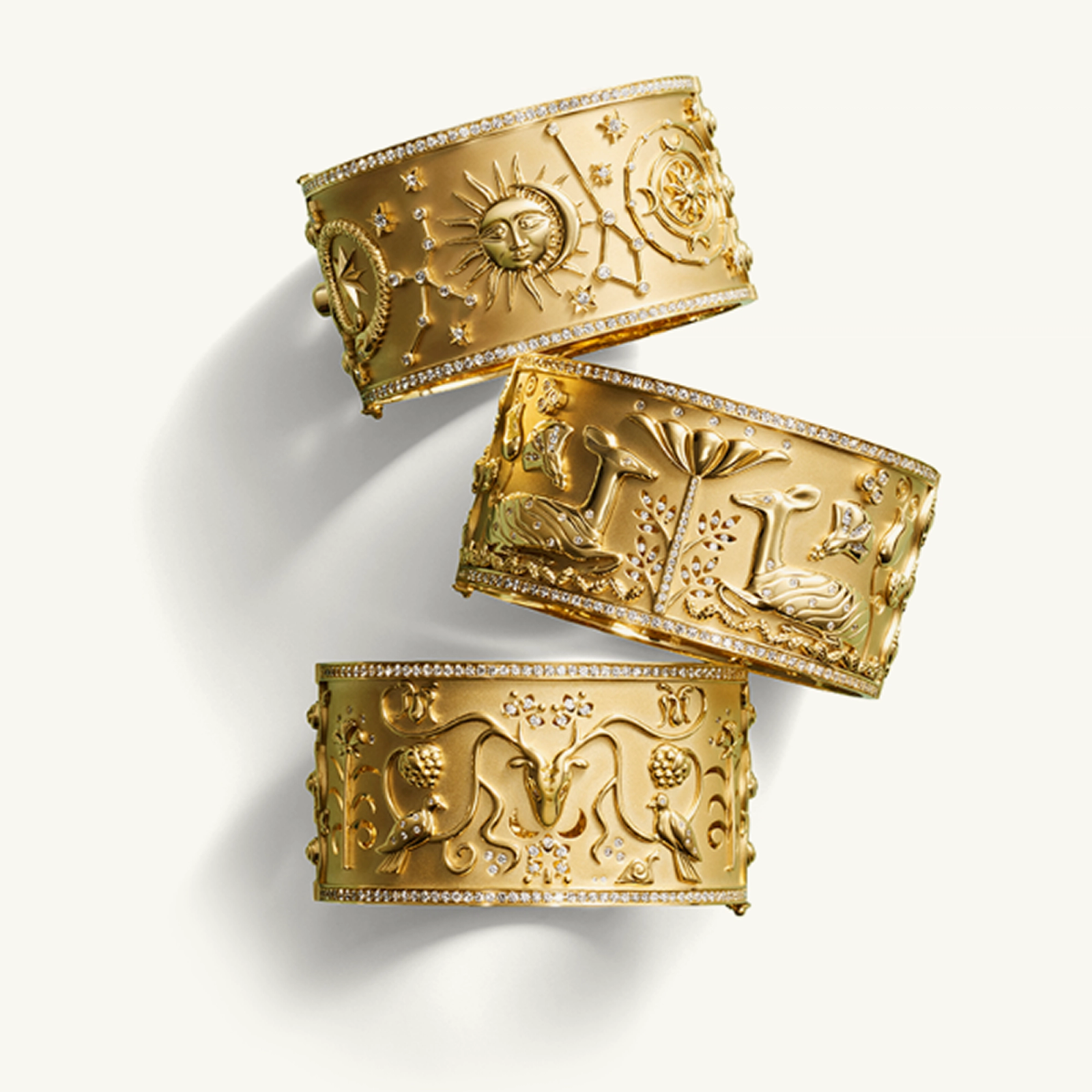 Three ornate gold cuffs embossed with celestial, animal, and floral designs, studded with diamonds.