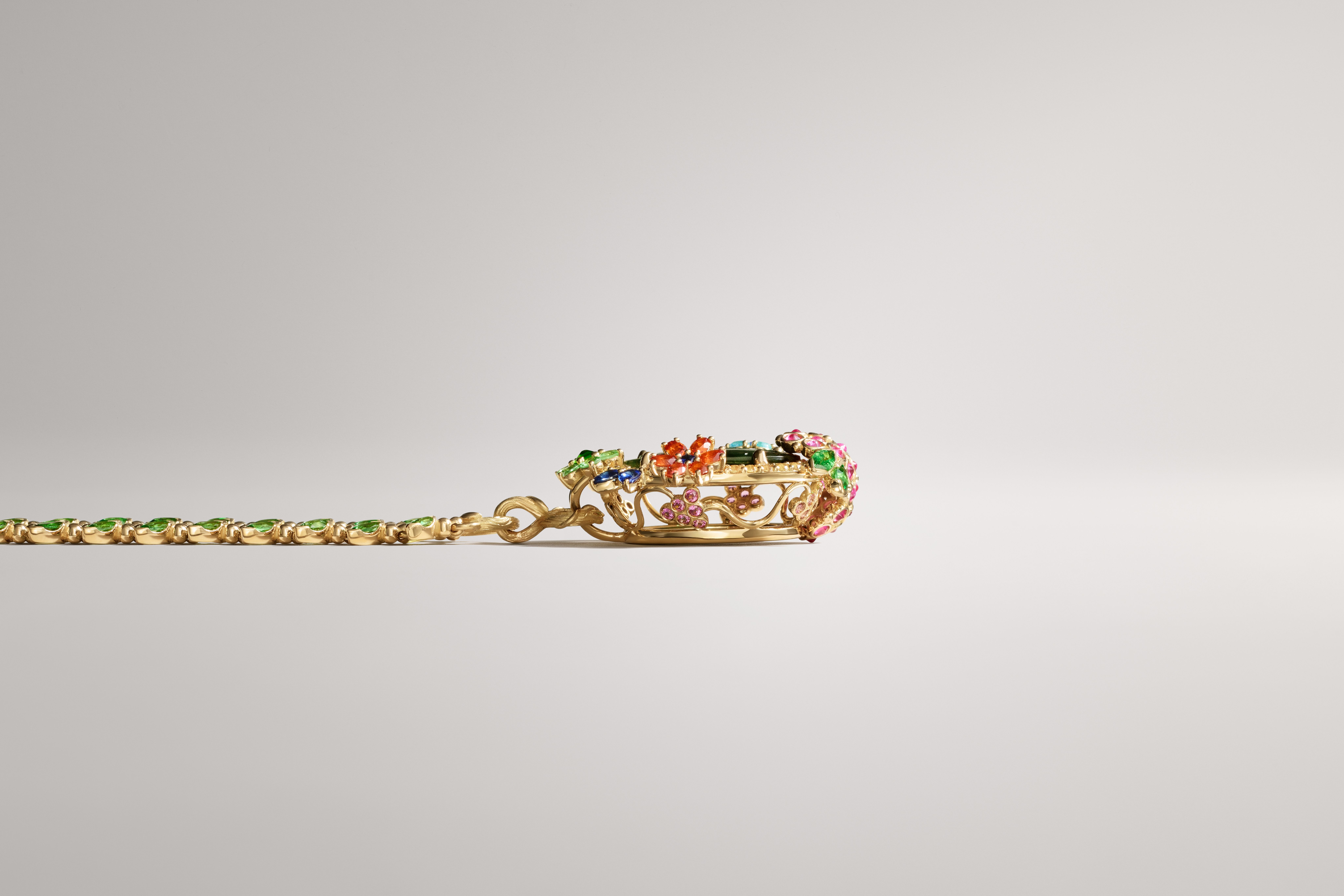 A gold chain with green gems connecting to an ornate gold centerpiece set with colorful gemstones.