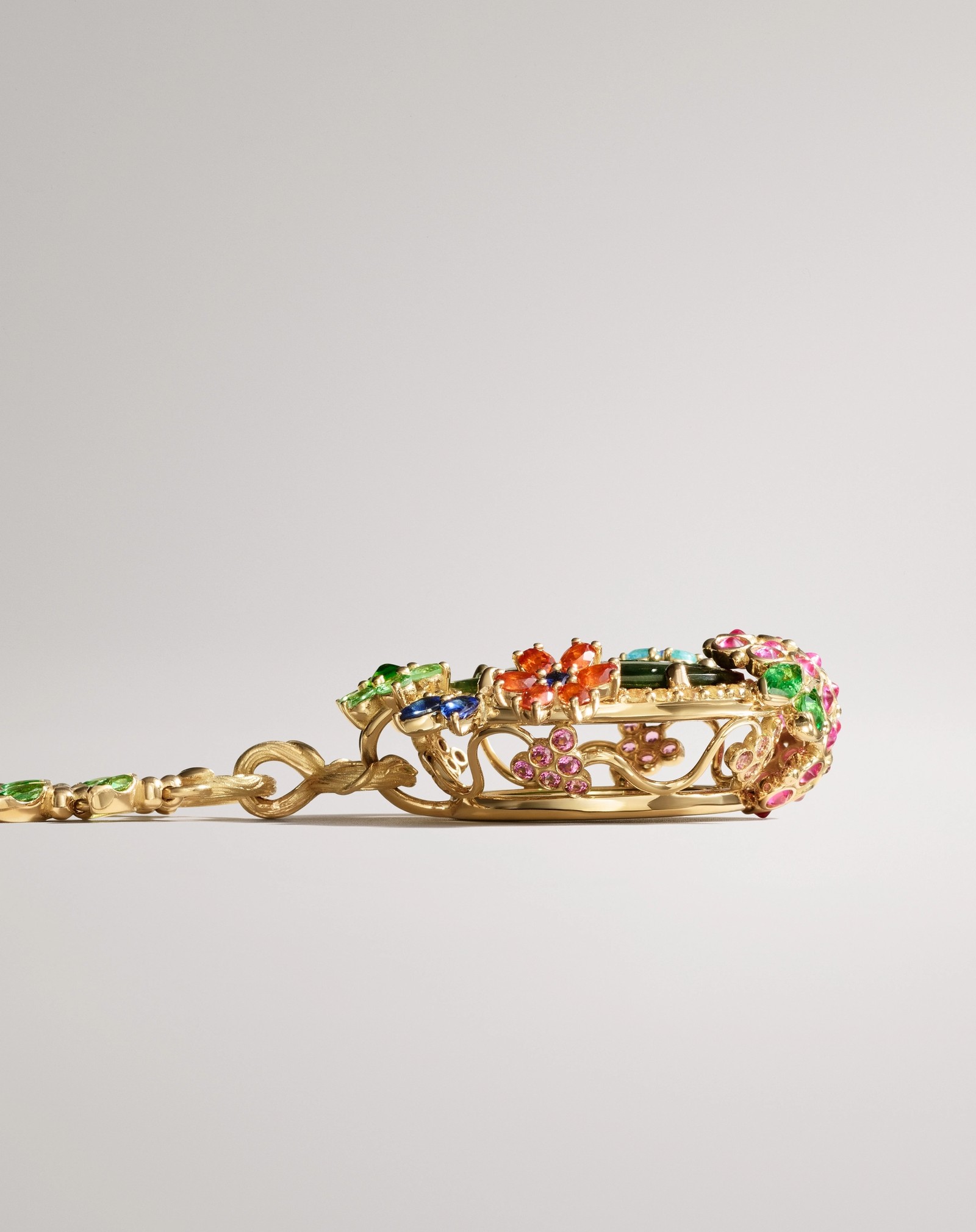 A gold chain with green gems connecting to an ornate gold centerpiece set with colorful gemstones.
