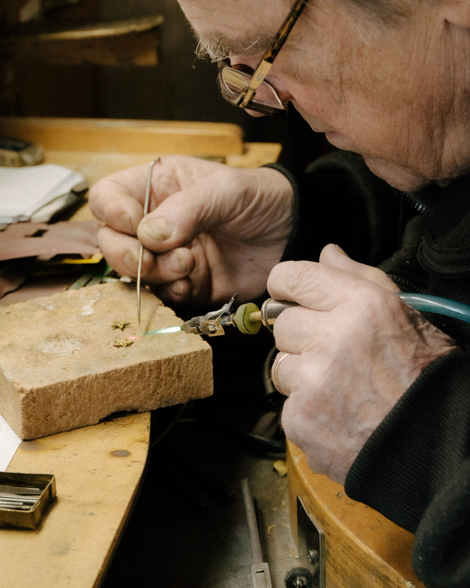 Close-up of a person with glasses soldering small metal pieces on a fire brick using a torch and a pick.