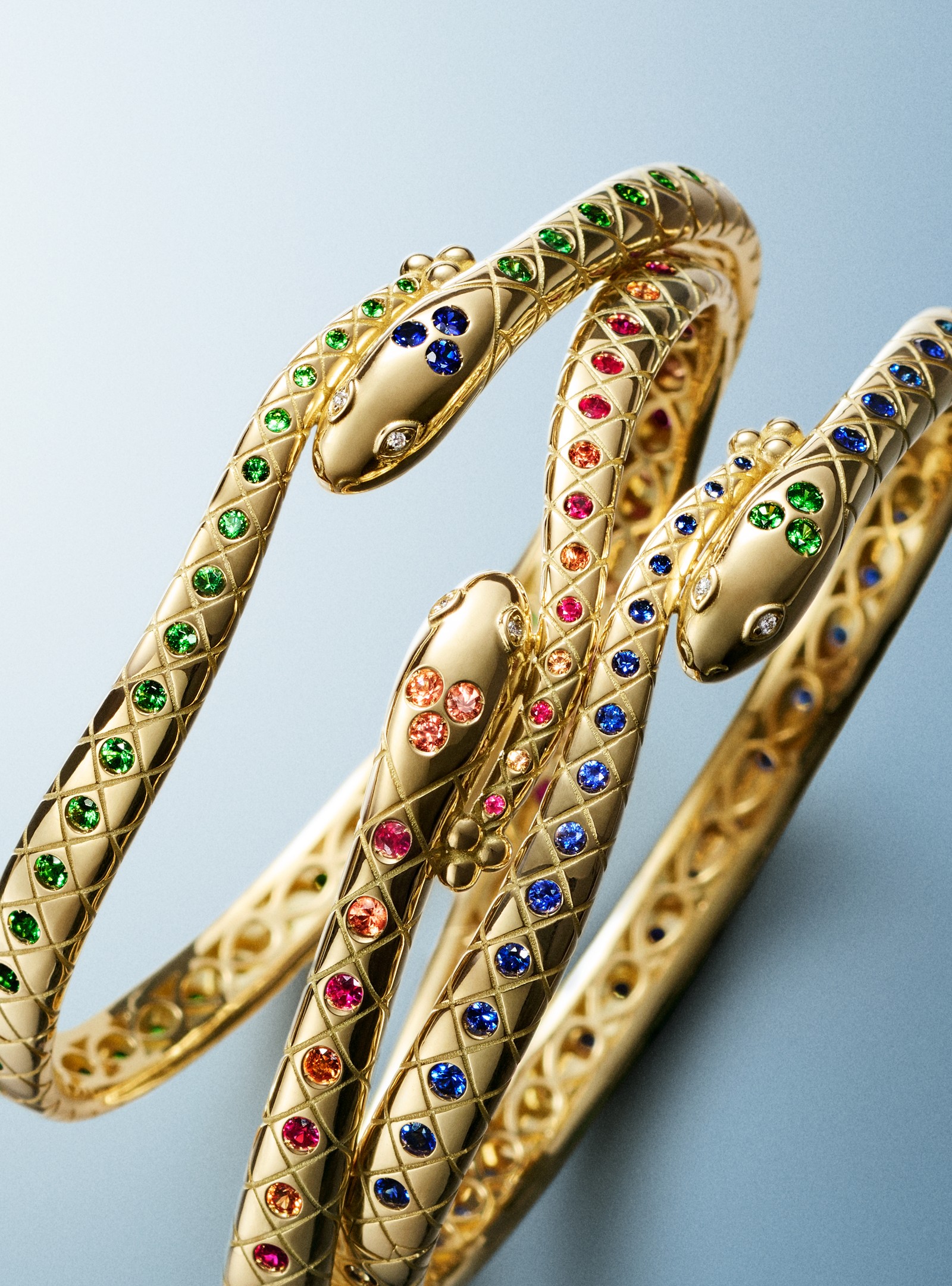 Three intertwined gold snake bracelets with green, red, and blue gemstones.