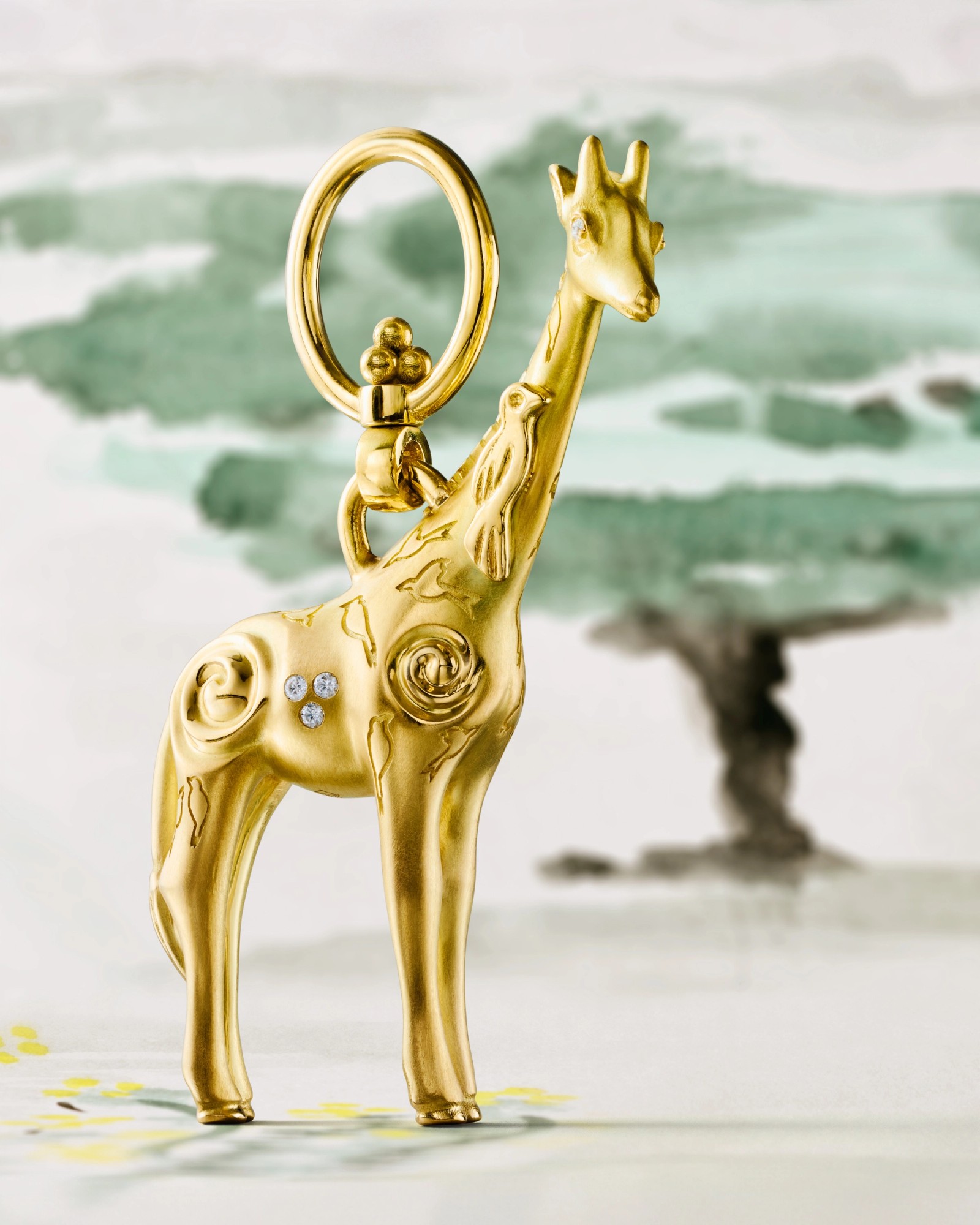 A golden giraffe charm with diamond details and swirling patterns stands against a blurred watercolor landscape.