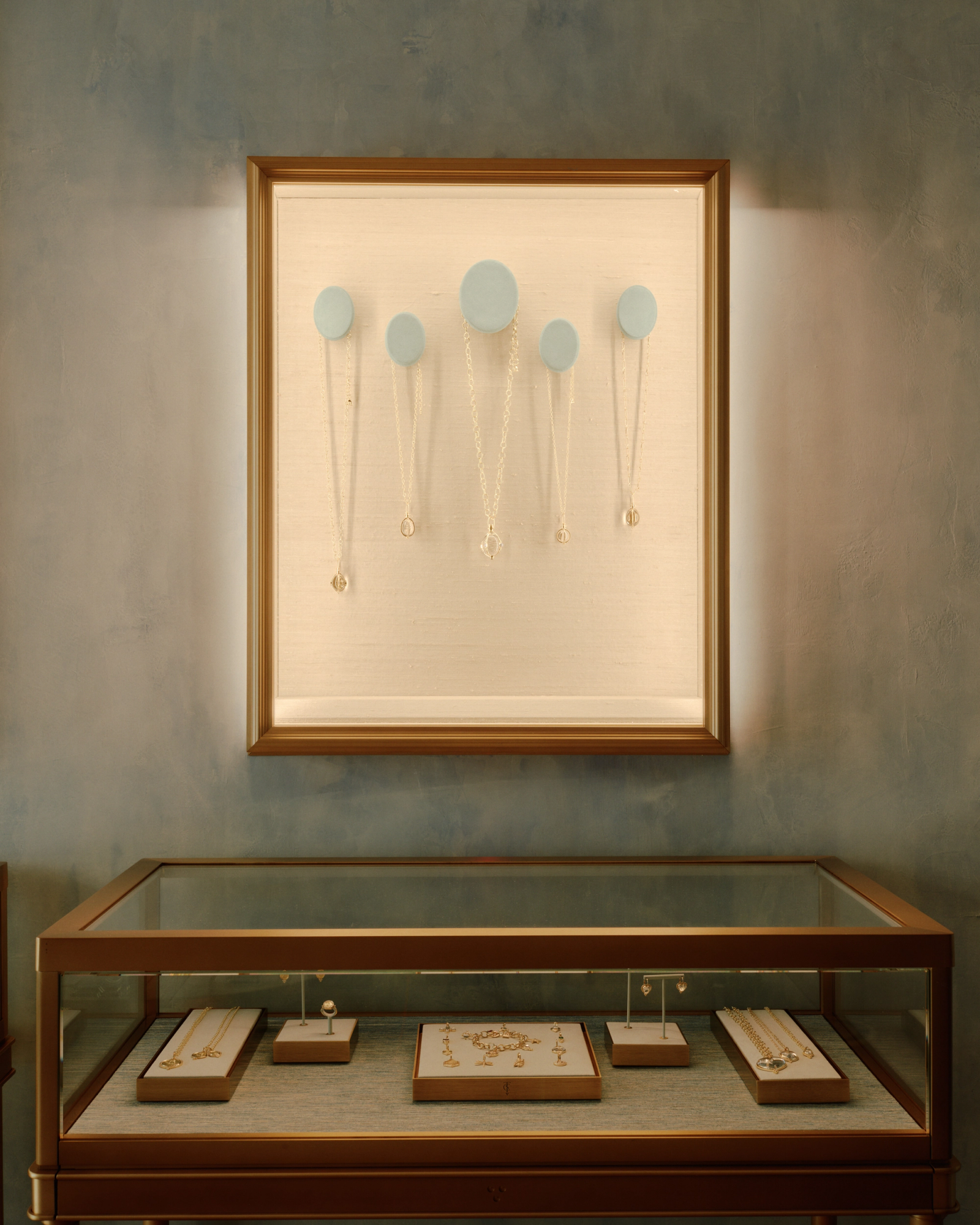 An illuminated wall display case with necklaces hangs above a glass counter filled with more jewelry.