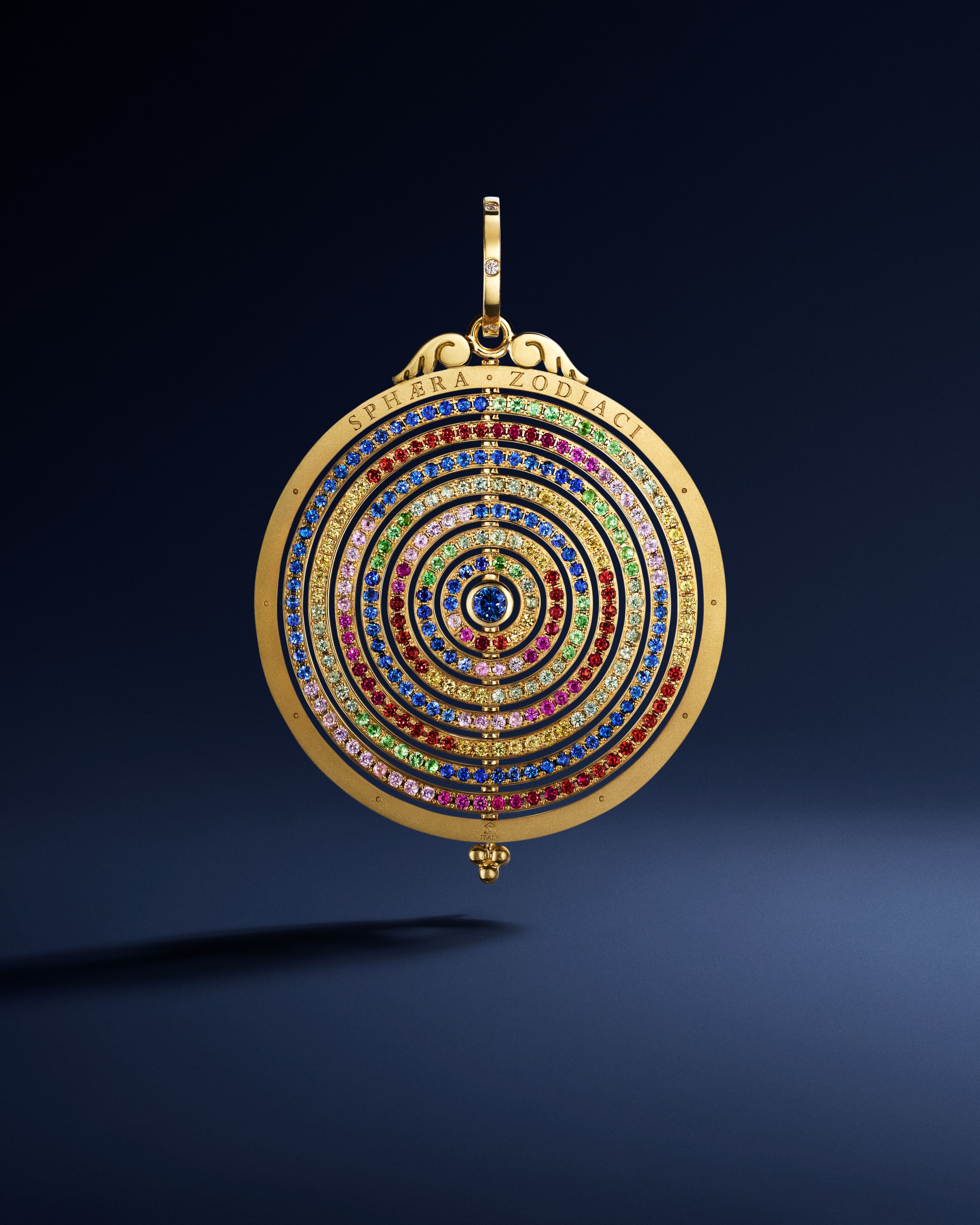 Gold circular pendant with concentric rings of colorful gemstones, inscribed 'SPHAERA ZODIACI'.
