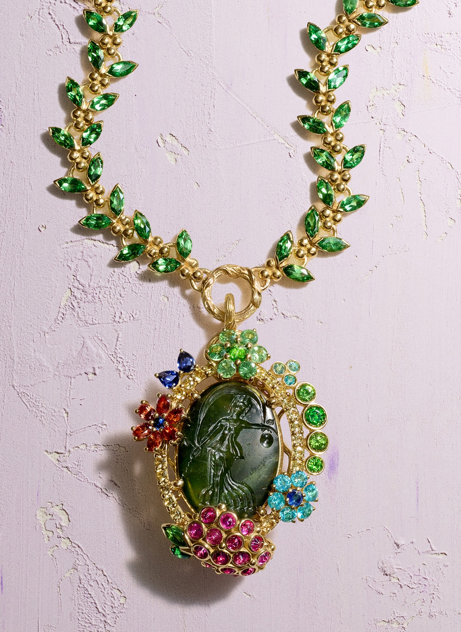 Gold necklace with green leaf gems and a dark green cameo pendant of a woman, surrounded by colorful gem flowers and a butterfly.