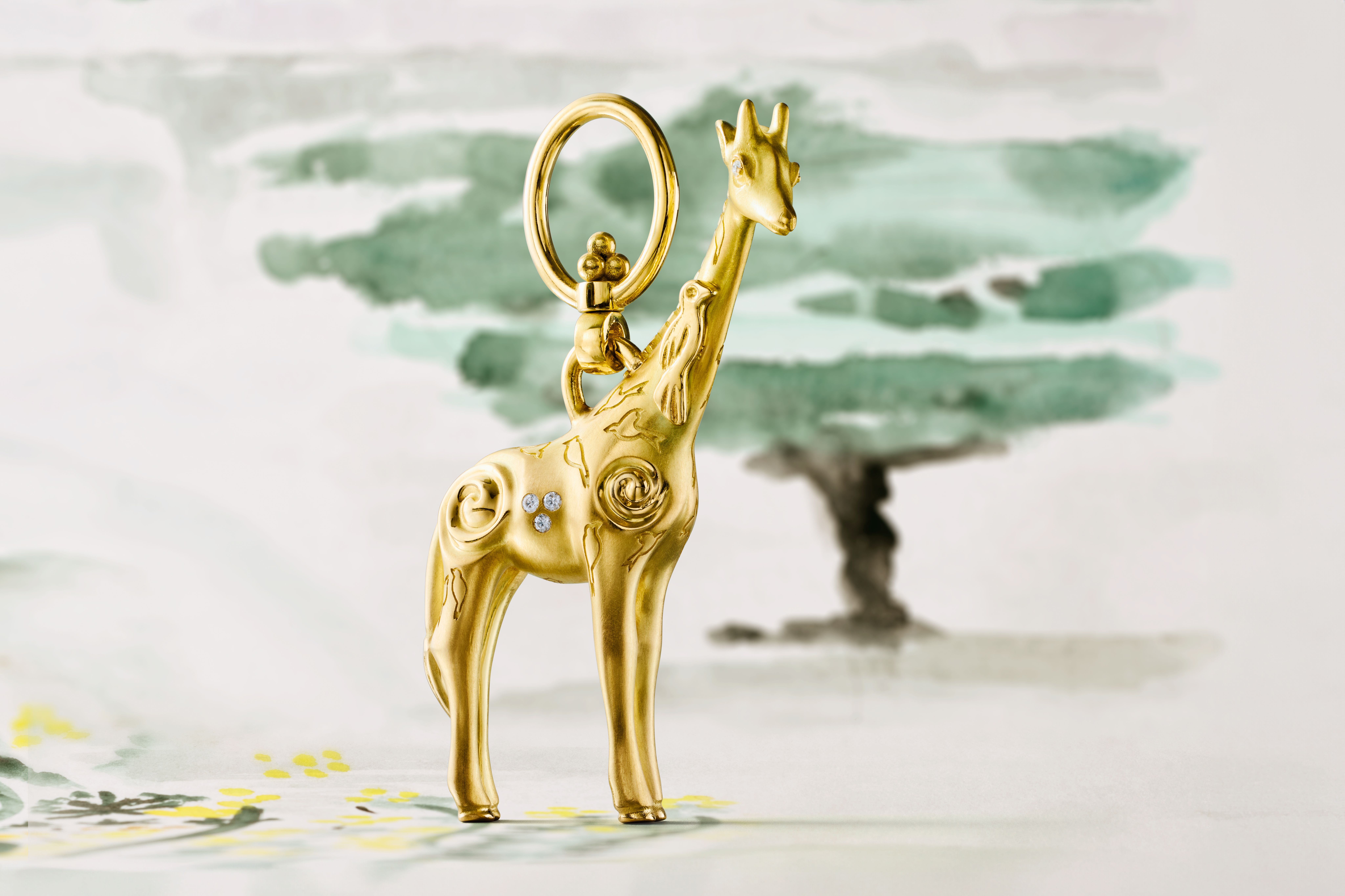 Golden giraffe charm with diamonds and swirling patterns against a watercolor landscape.