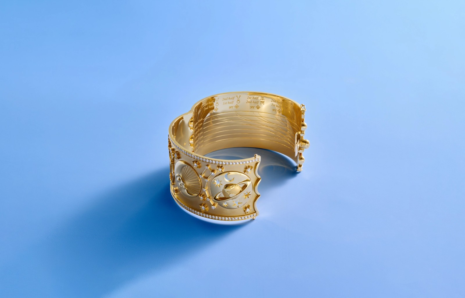 Ornate gold cuff bracelet with celestial designs and small gems, resting on a blue background.